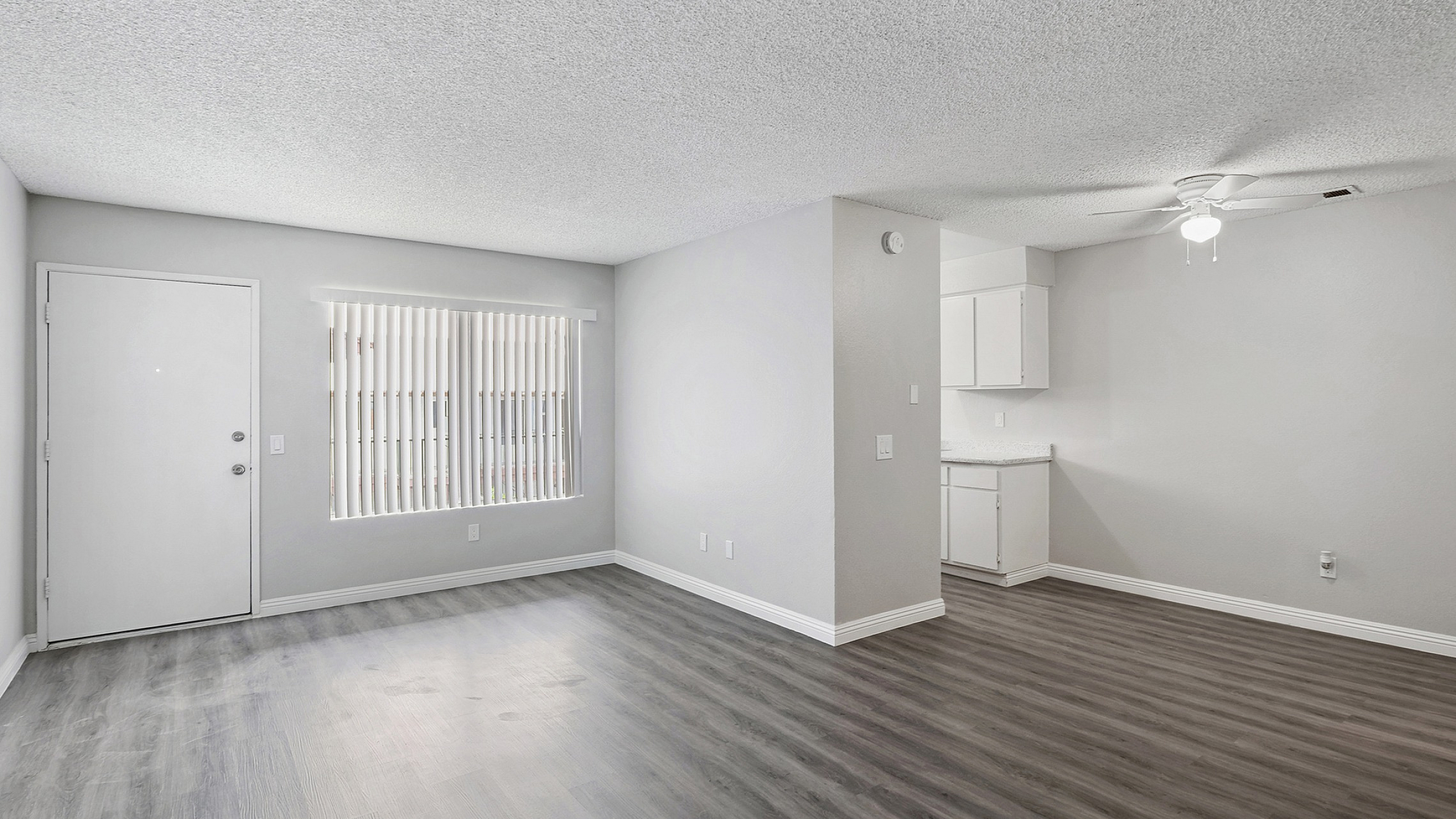 Bright and modern living area with sleek gray flooring, ample natural light through large windows, and a cozy kitchen nook.