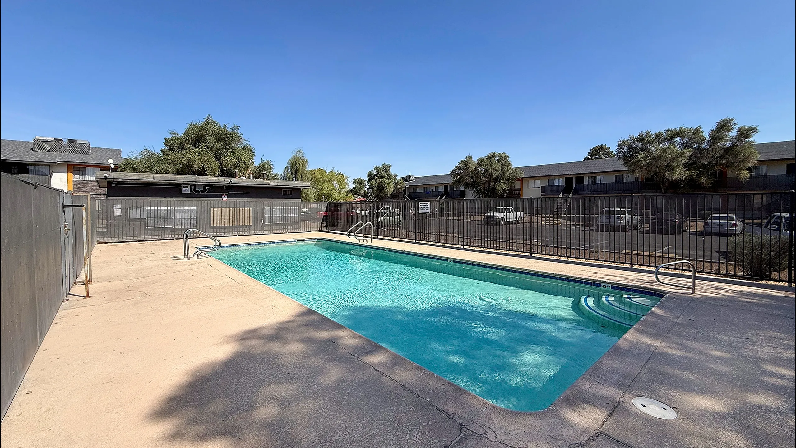 Inviting outdoor pool area with crystal-clear water, surrounded by a secure fence and shaded by mature trees, perfect for relaxation or entertainment.