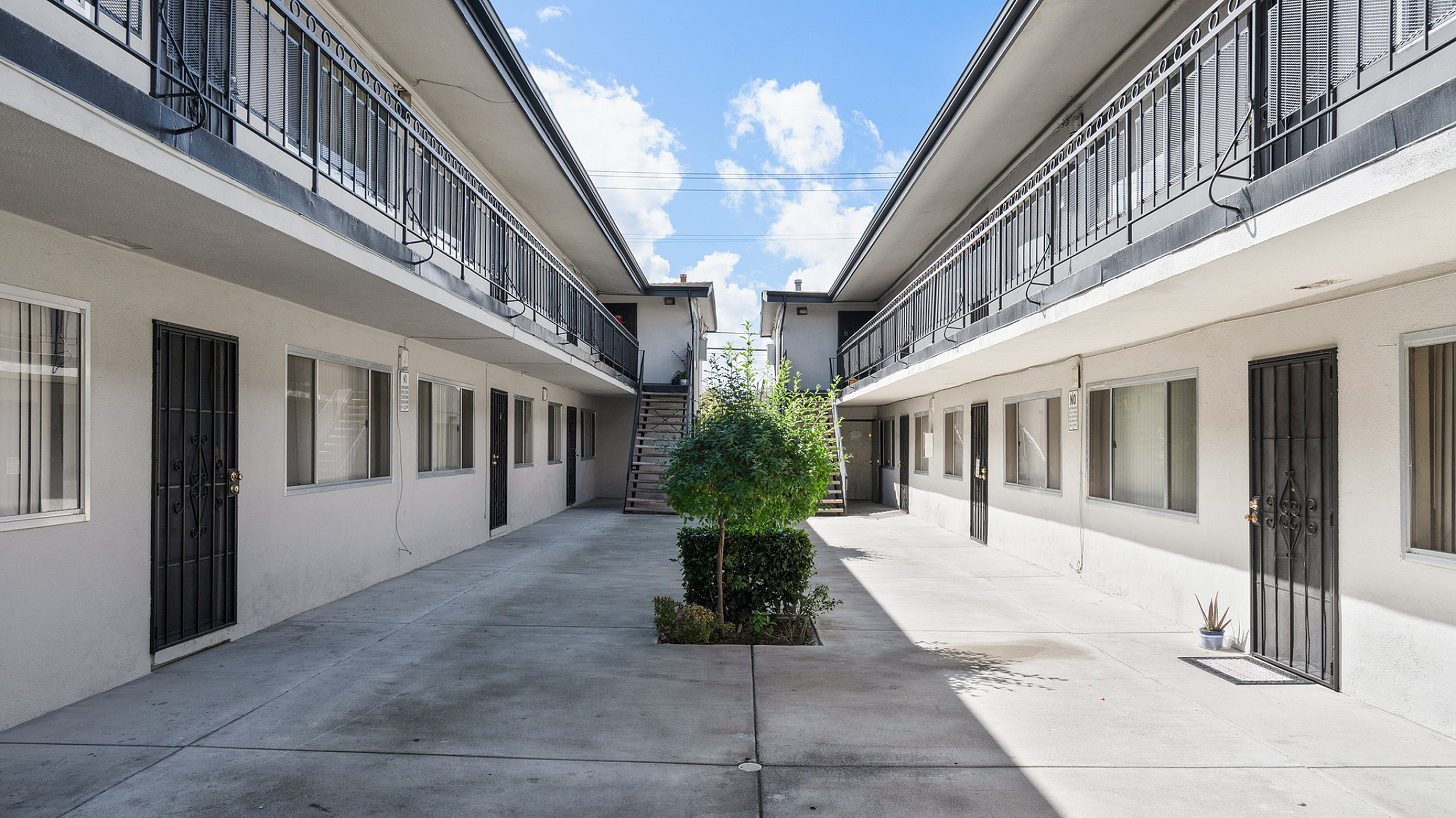 Charming courtyard view of a modern apartment complex with sleek railings, vibrant greenery, and a bright sky backdrop.