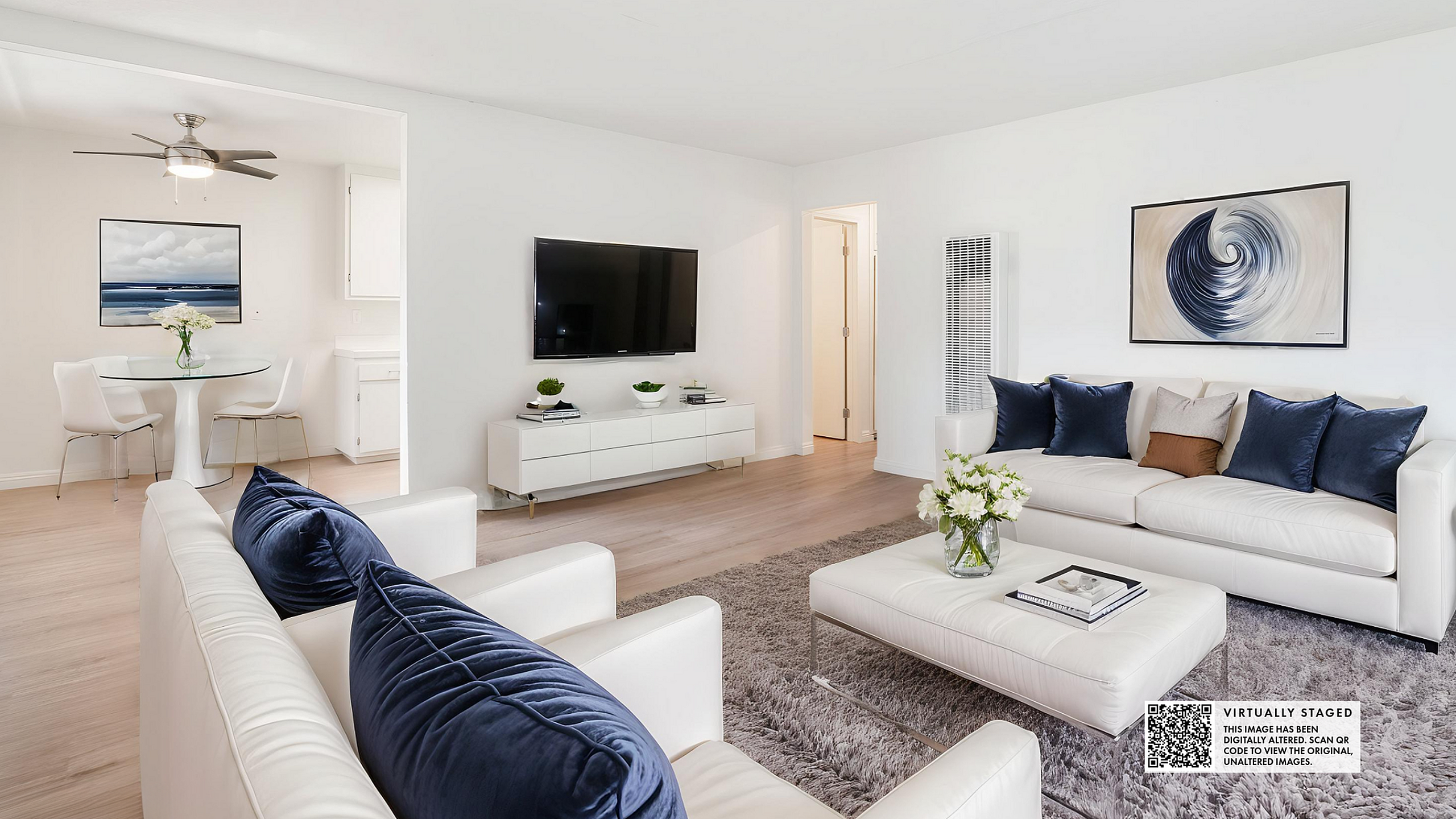 Elegant living room with plush white sofas, navy blue accent pillows, and a chic glass coffee table. Bright dining area with modern table set and artistic wall decor.