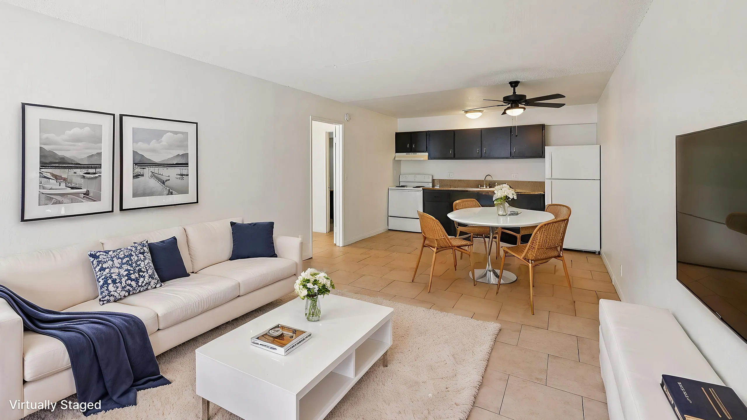 Elegant, virtually staged open-concept living room with white sofa, modern decor, and dining area leading to a sleek kitchen.