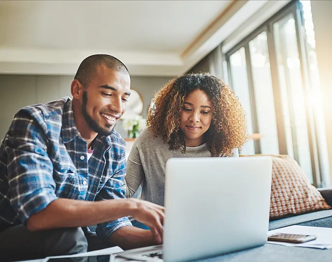 Happy couple working on a laptop in a bright, modern living room with large windows bringing in natural light.