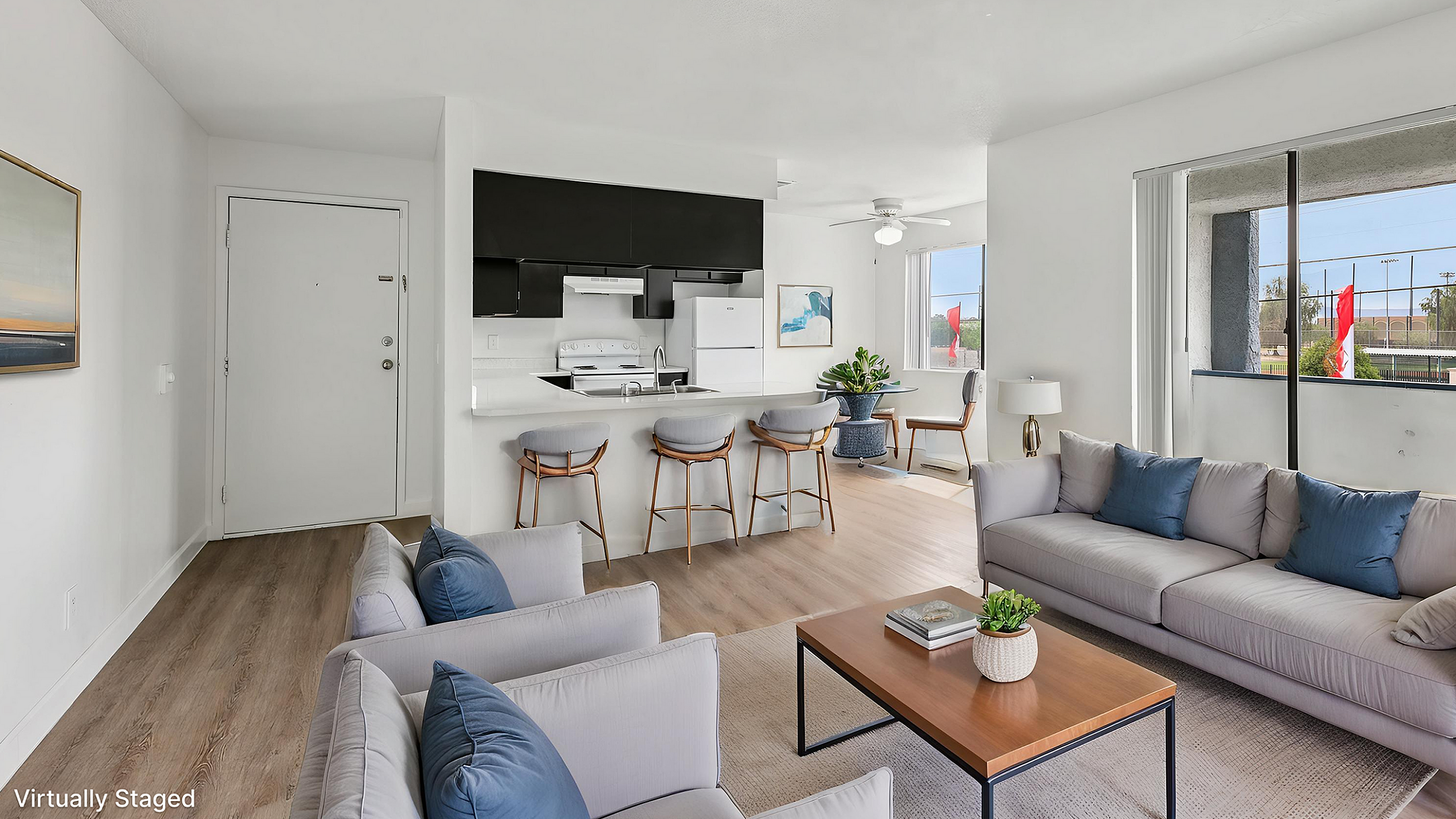 Modern living room with stylish furniture, open kitchen area, and large windows providing natural light, in a virtually staged apartment.