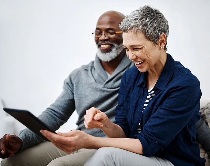 Happy couple enjoying a cozy moment at home, sharing a laugh while looking at a tablet.
