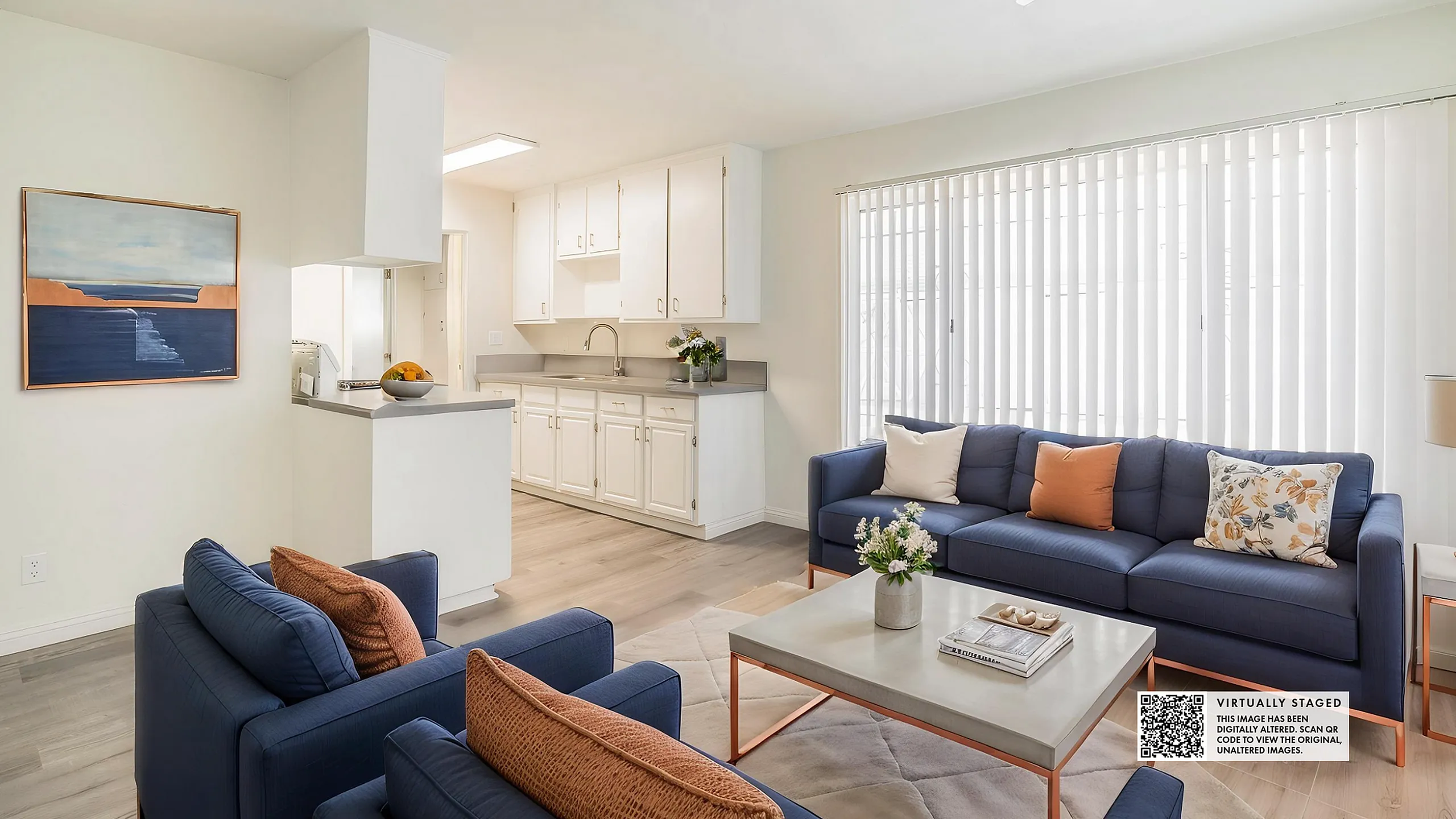 Bright and inviting open-concept living room featuring modern blue sofas, elegant d&eacute;cor, and a cozy kitchen with contemporary cabinetry.