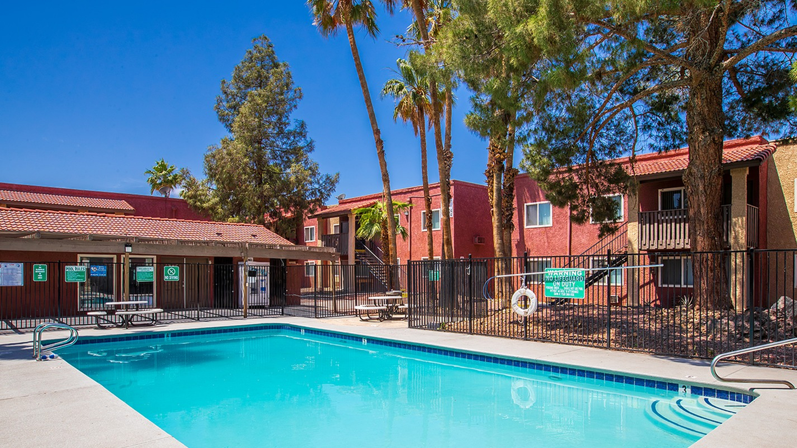 Inviting outdoor pool area with turquoise water, surrounded by lush palm trees and charming apartment buildings.