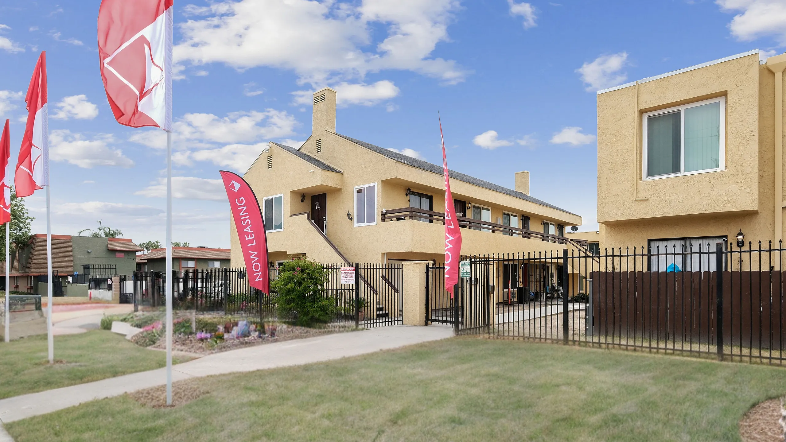 Charming apartment complex with modern design, highlighted by vibrant flags and lush landscaping, now leasing.