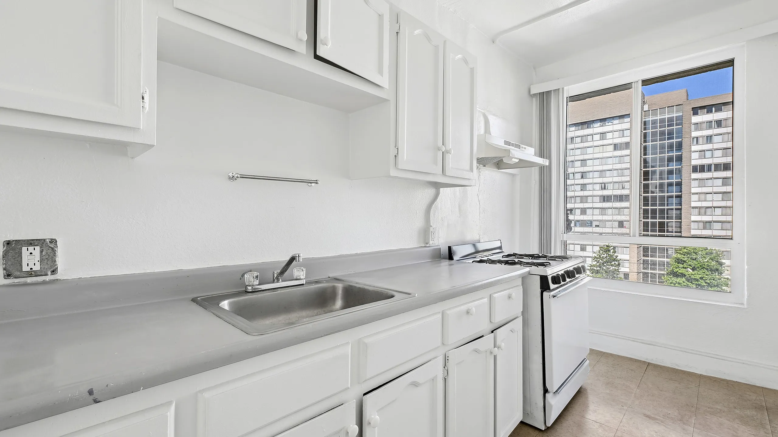 Bright kitchen with sleek countertops, modern white cabinetry, and large window offering a scenic cityscape view.