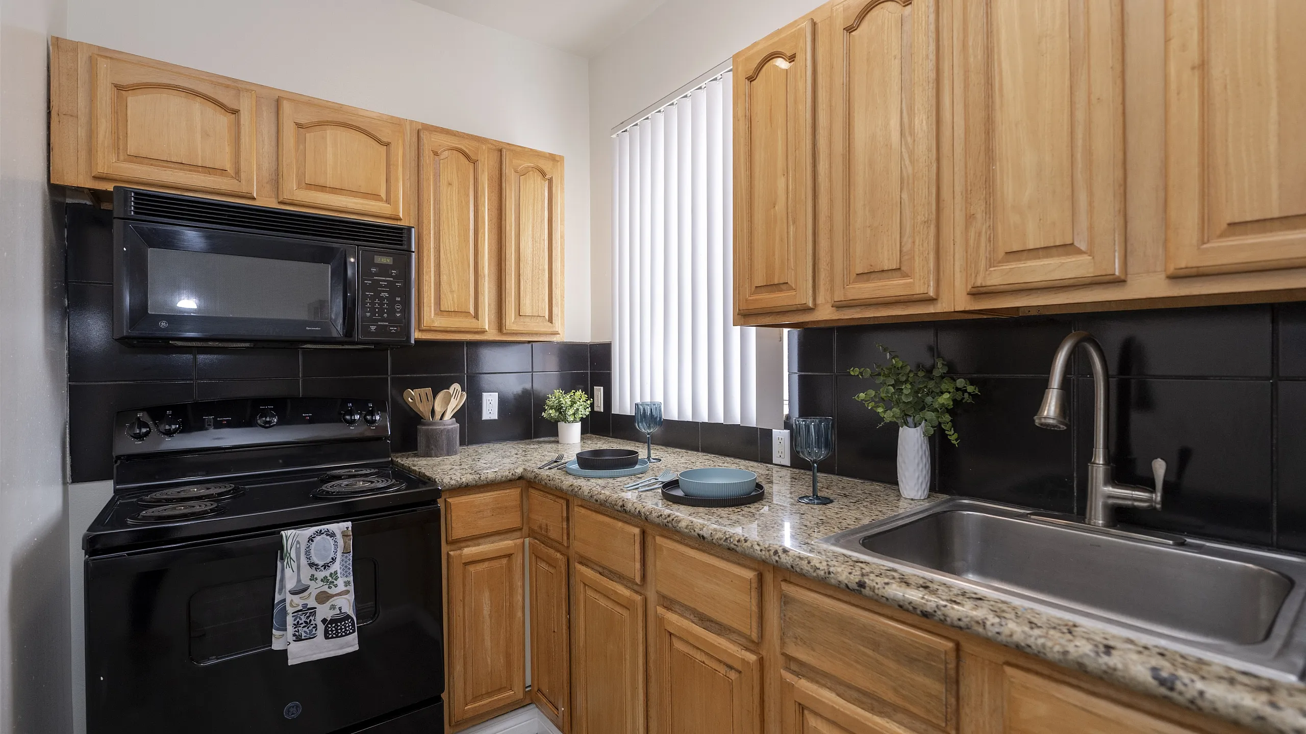 Modern kitchen with wooden cabinets, sleek black appliances, granite countertops, and elegant decor.