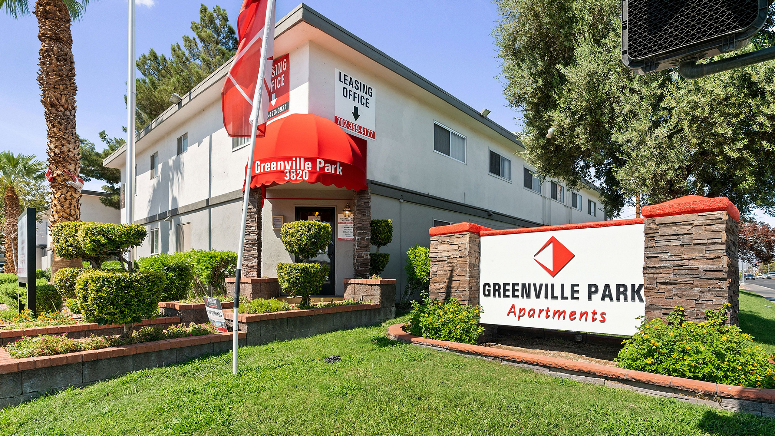 Welcoming exterior of Greenville Park Apartments with lush landscaping, prominently featuring the leasing office under a vibrant red canopy.
