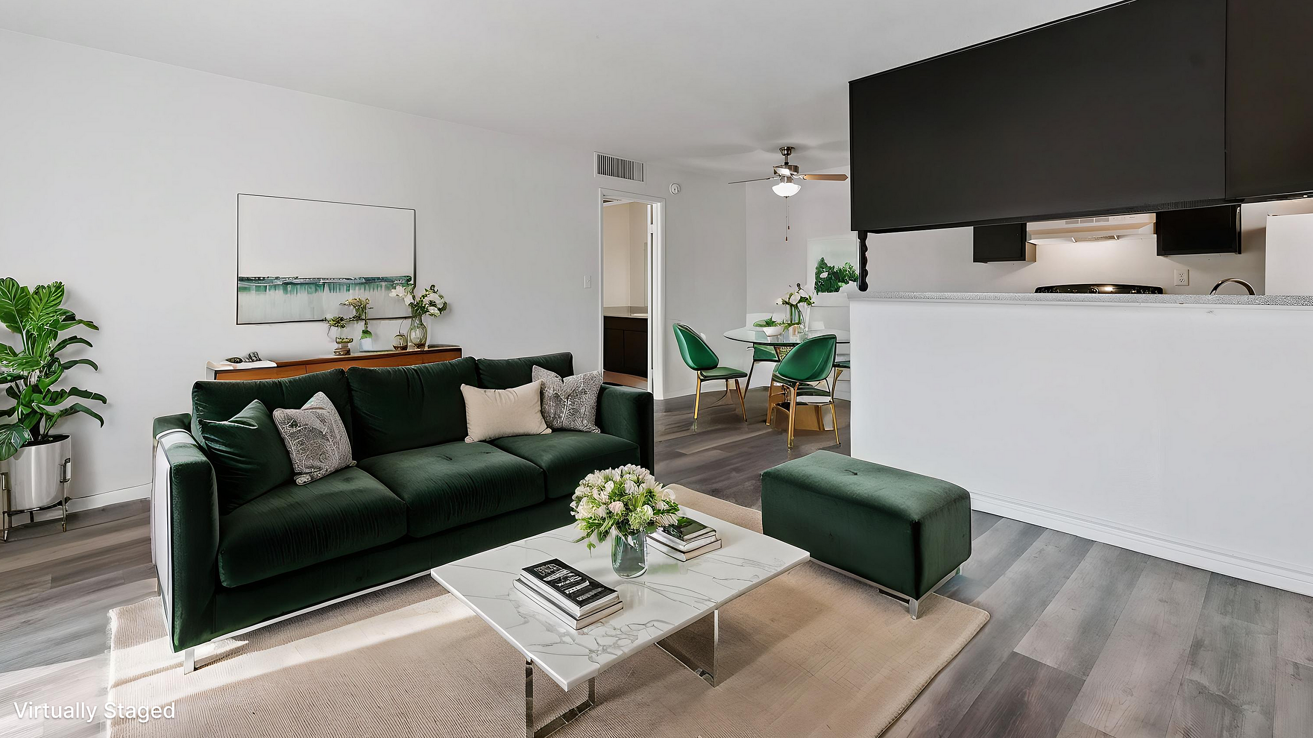Sleek and modern living room with a stylish dark green sofa, elegant marble coffee table, and vibrant indoor plants, leading to a chic dining area with green chairs.