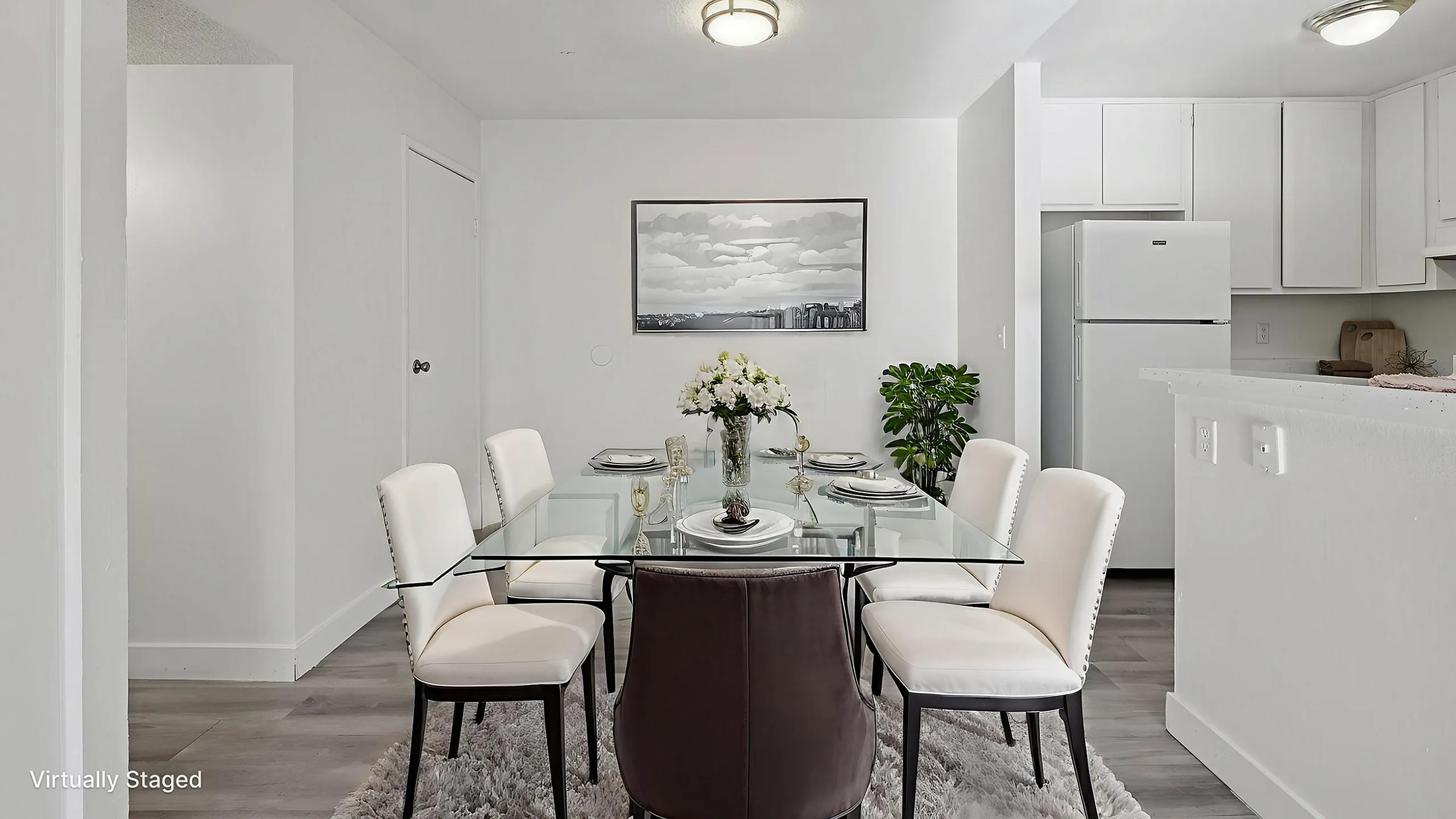 Chic dining area with a glass table set for four, adjacent to a sleek modern kitchen. Bright and airy ambiance with stylish decor.