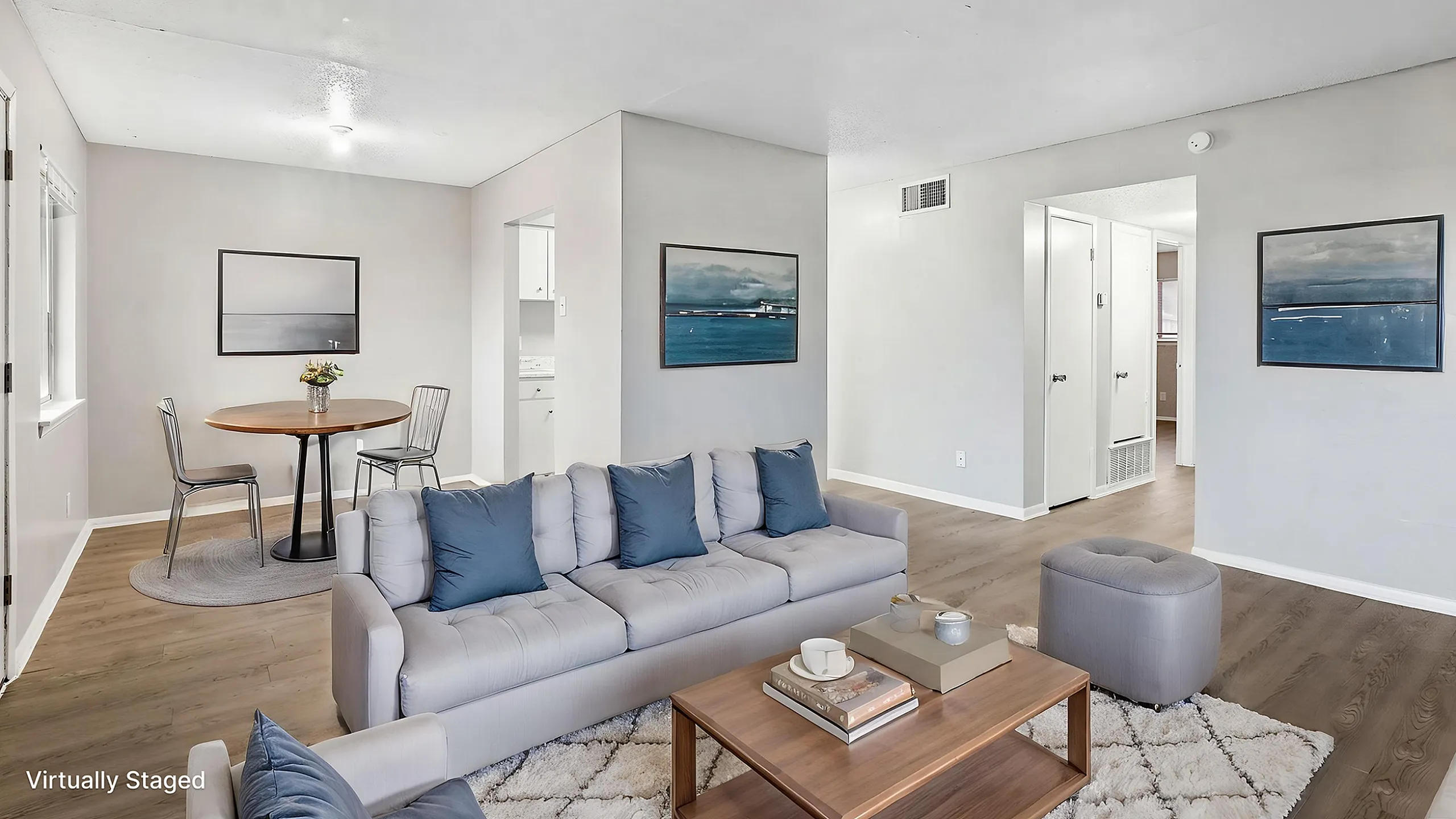 Virtually staged living room with chic gray sofa, elegant coffee table, and cozy dining nook highlighting modern interior design.