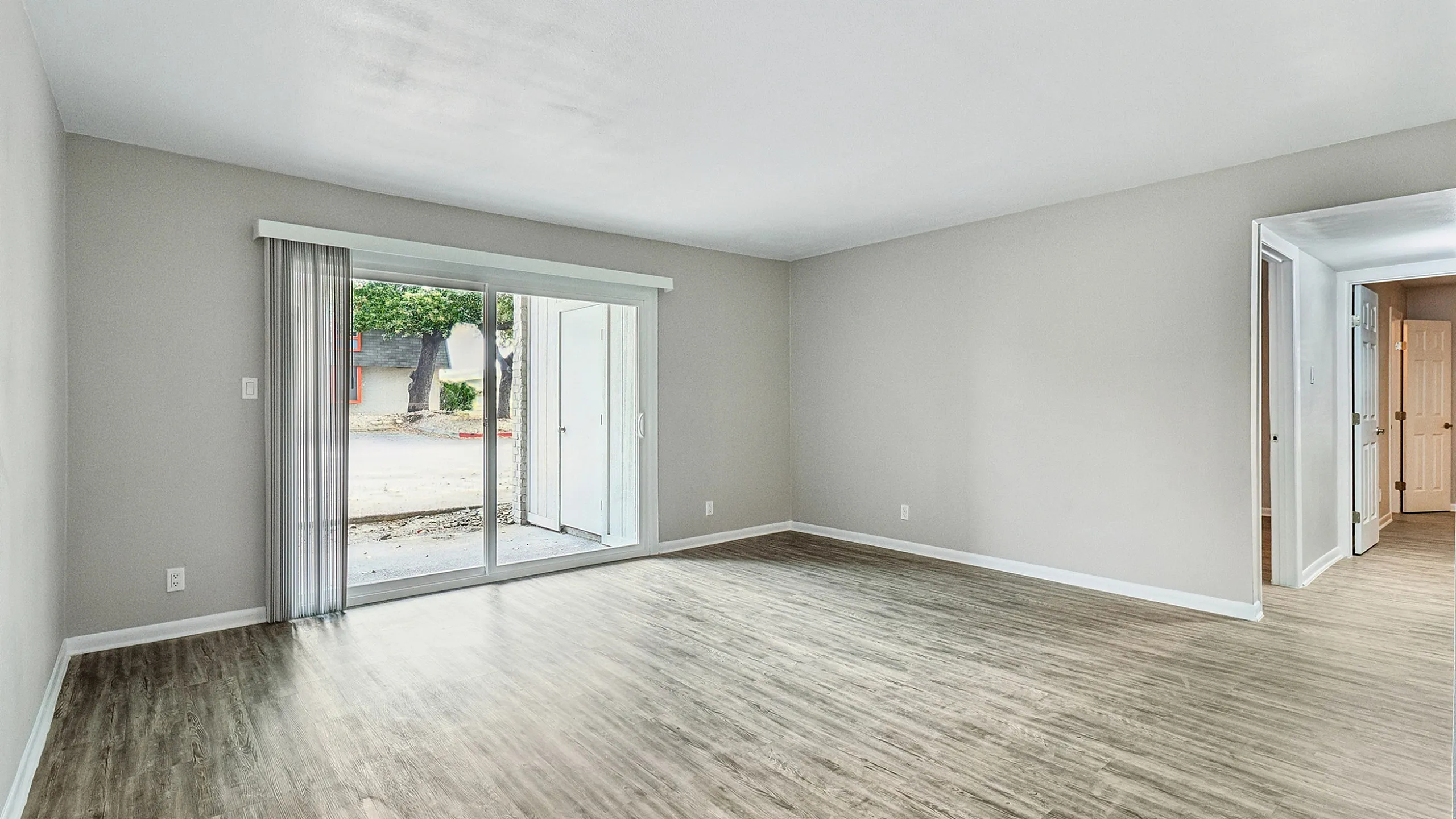 Bright and spacious living room with sleek hardwood floors and large sliding glass doors leading to a serene outdoor space.