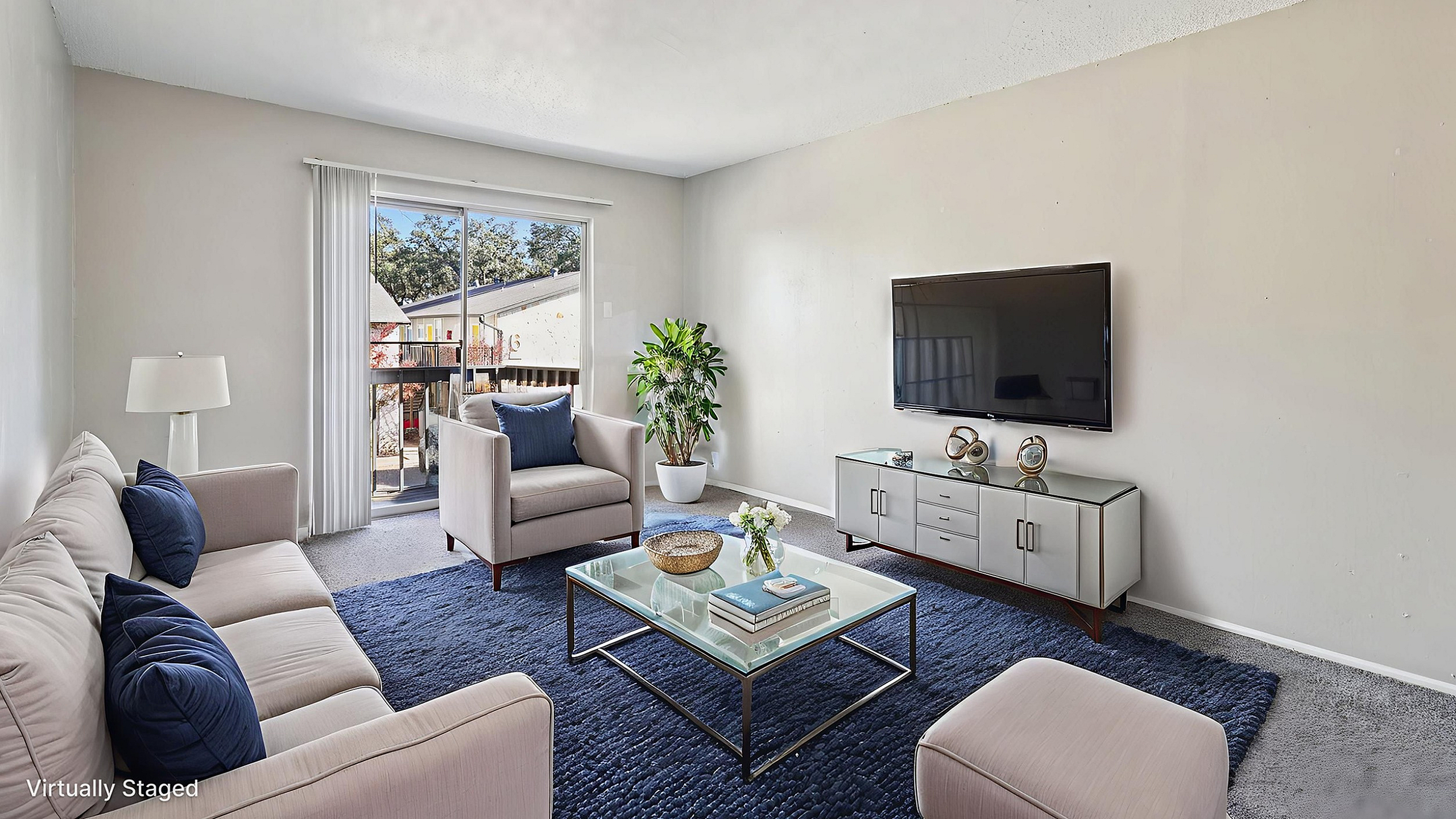 Bright, modern living room with elegant furniture, large sliding windows, and a serene view, featuring a stylish glass coffee table and plush seating.