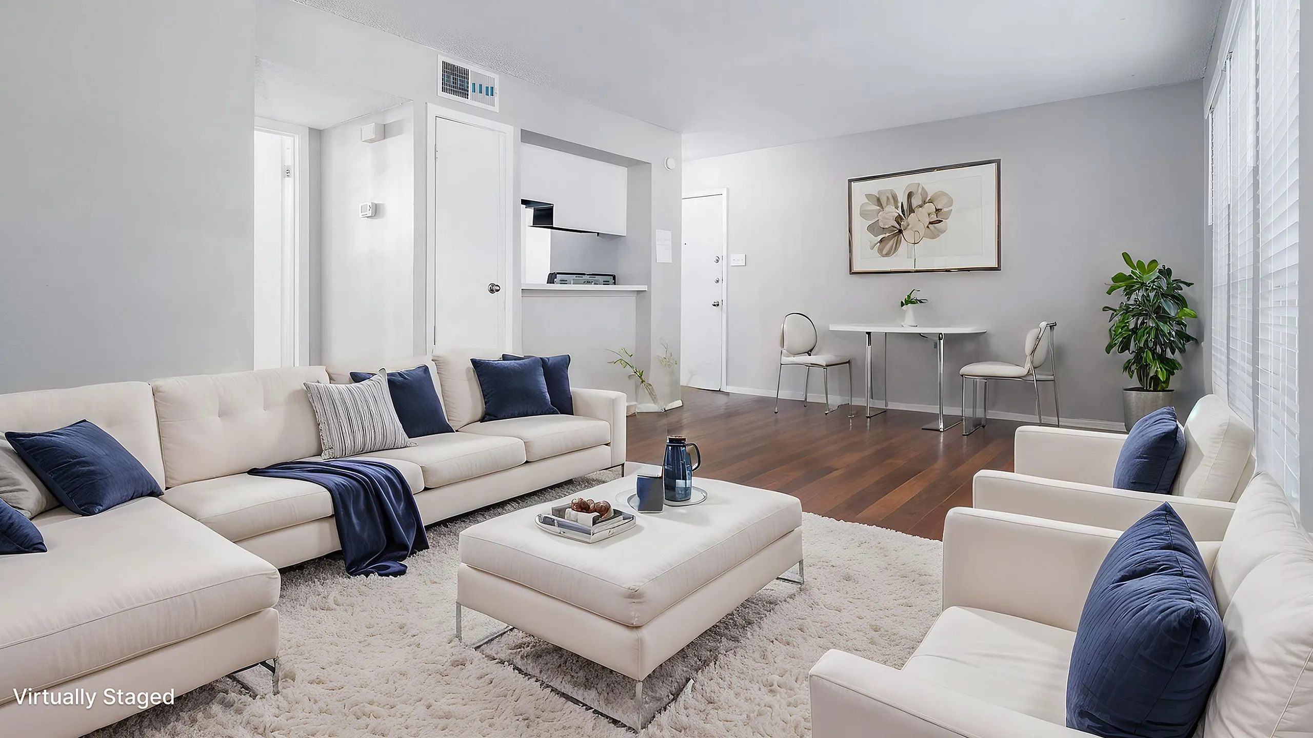 Bright and inviting living room with plush white furniture, accentuated by dark blue cushions, complementing a sleek dining area in a modern open-plan design.