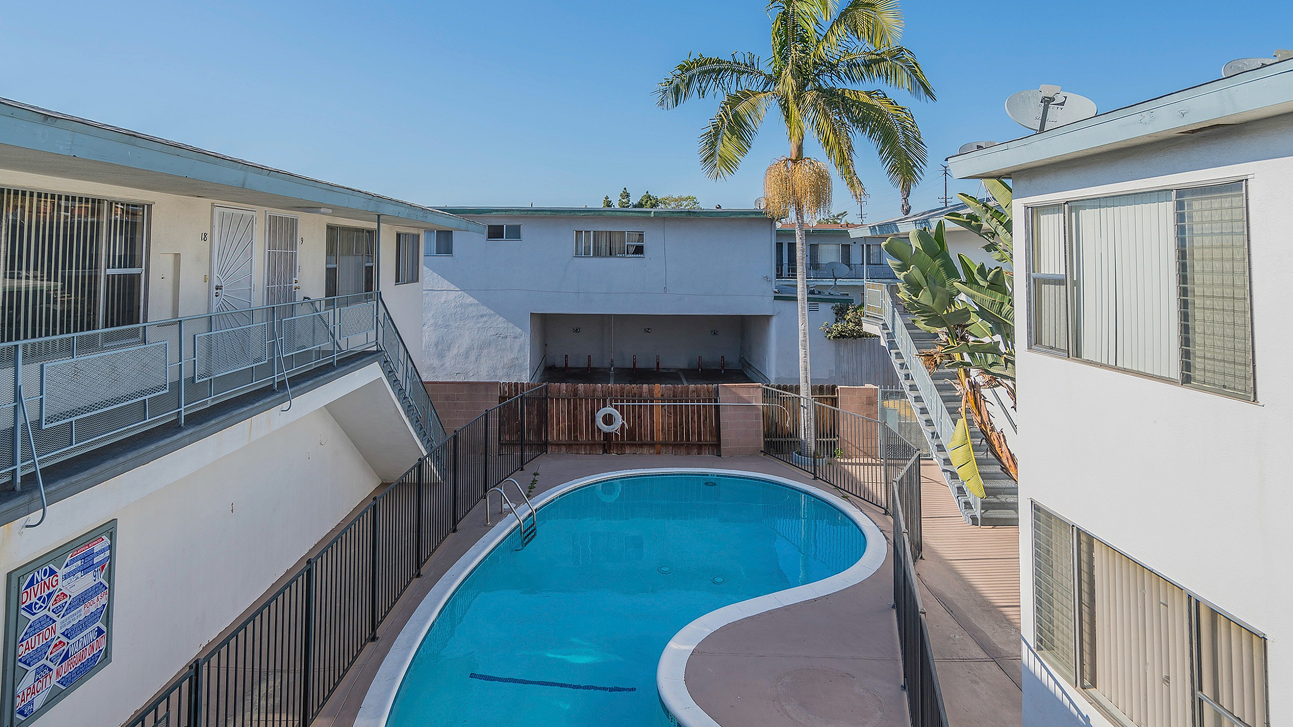 Inviting apartment courtyard with a sparkling pool surrounded by modern white buildings and lush palm trees.