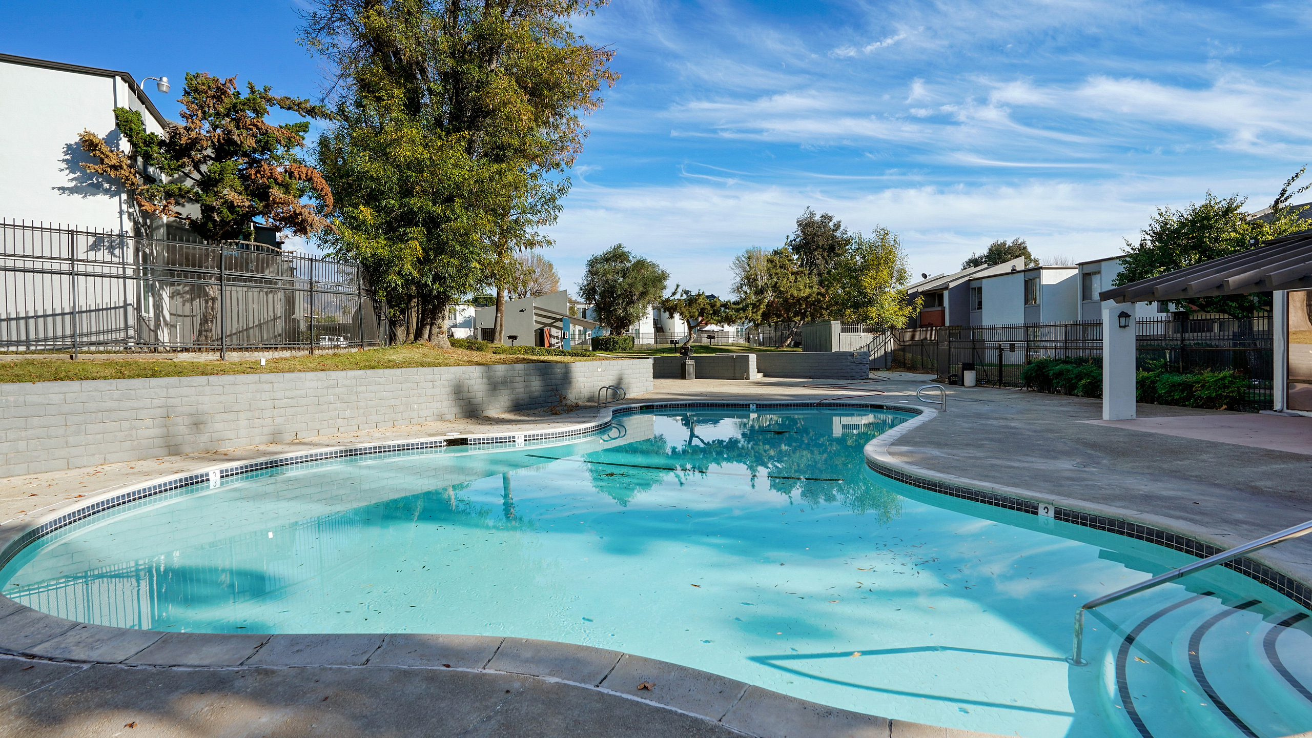 Inviting outdoor pool area with crystal-clear water, surrounded by lush greenery and modern architecture under a bright blue sky.