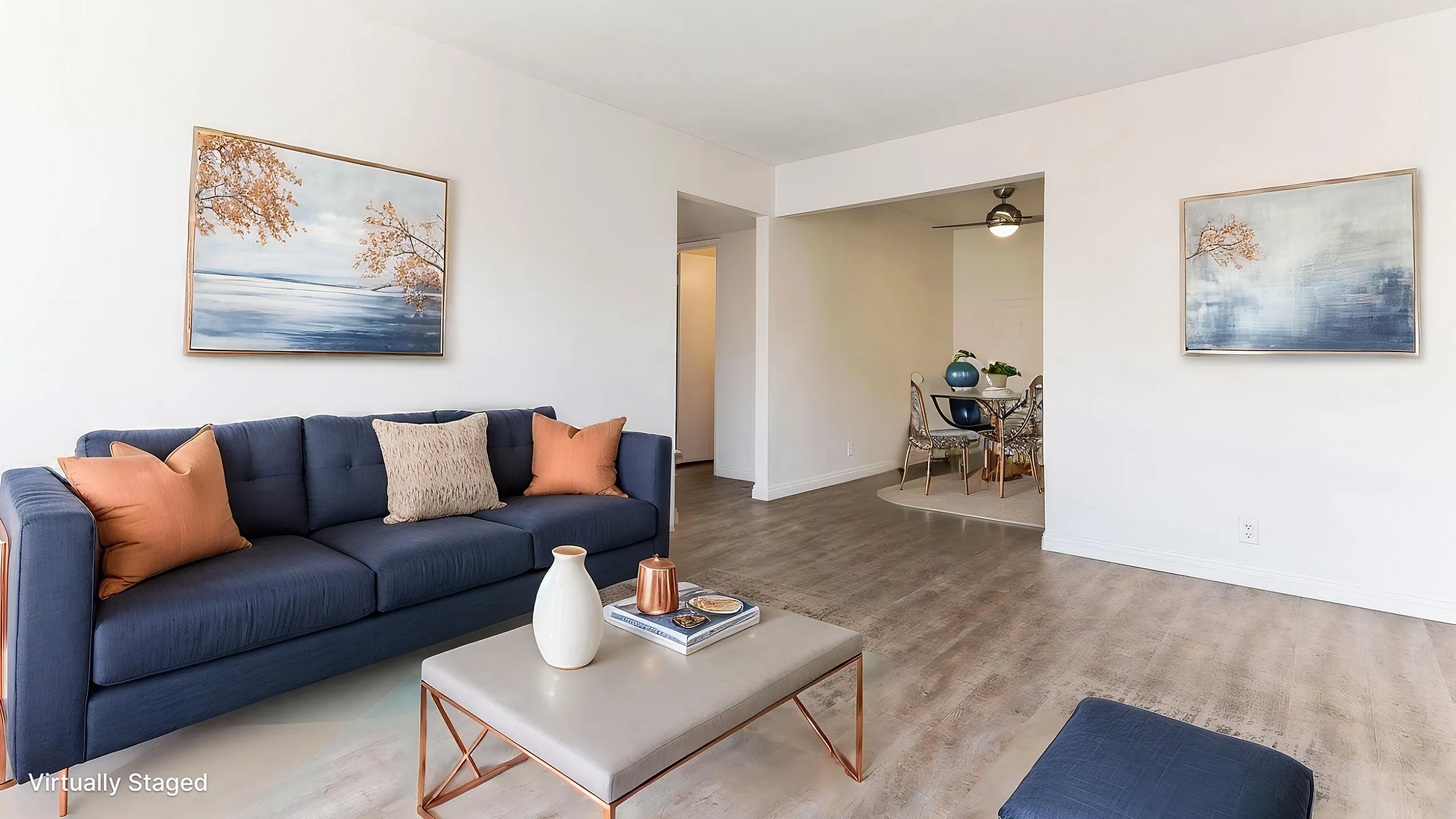 Modern living room with chic navy sofa, vibrant orange cushions, and elegant wall art, opening into a dining area with stylish chairs.