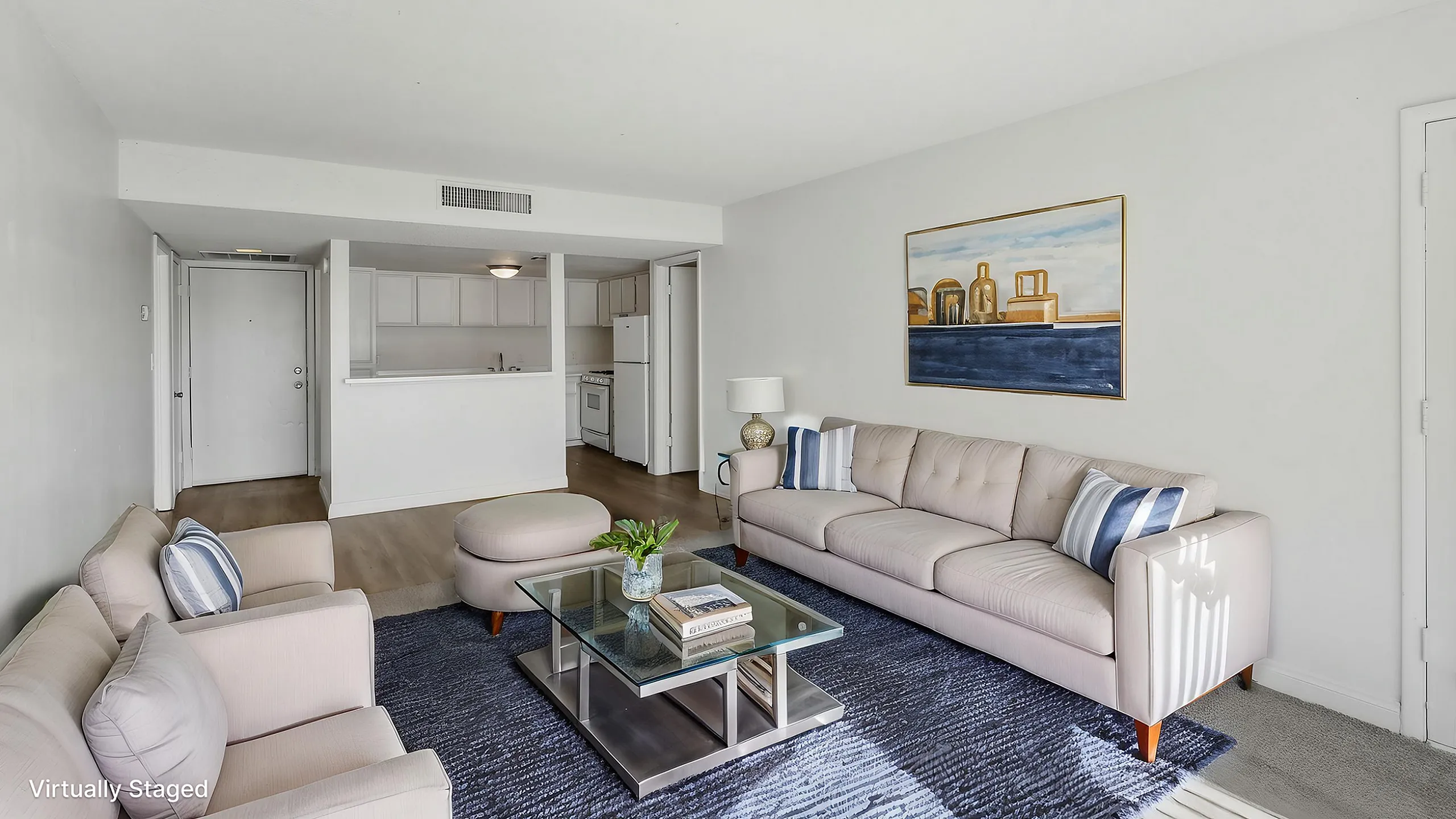 Contemporary living room with plush beige sofas, a chic glass coffee table, and a serene wall painting, offering a welcoming and airy atmosphere.