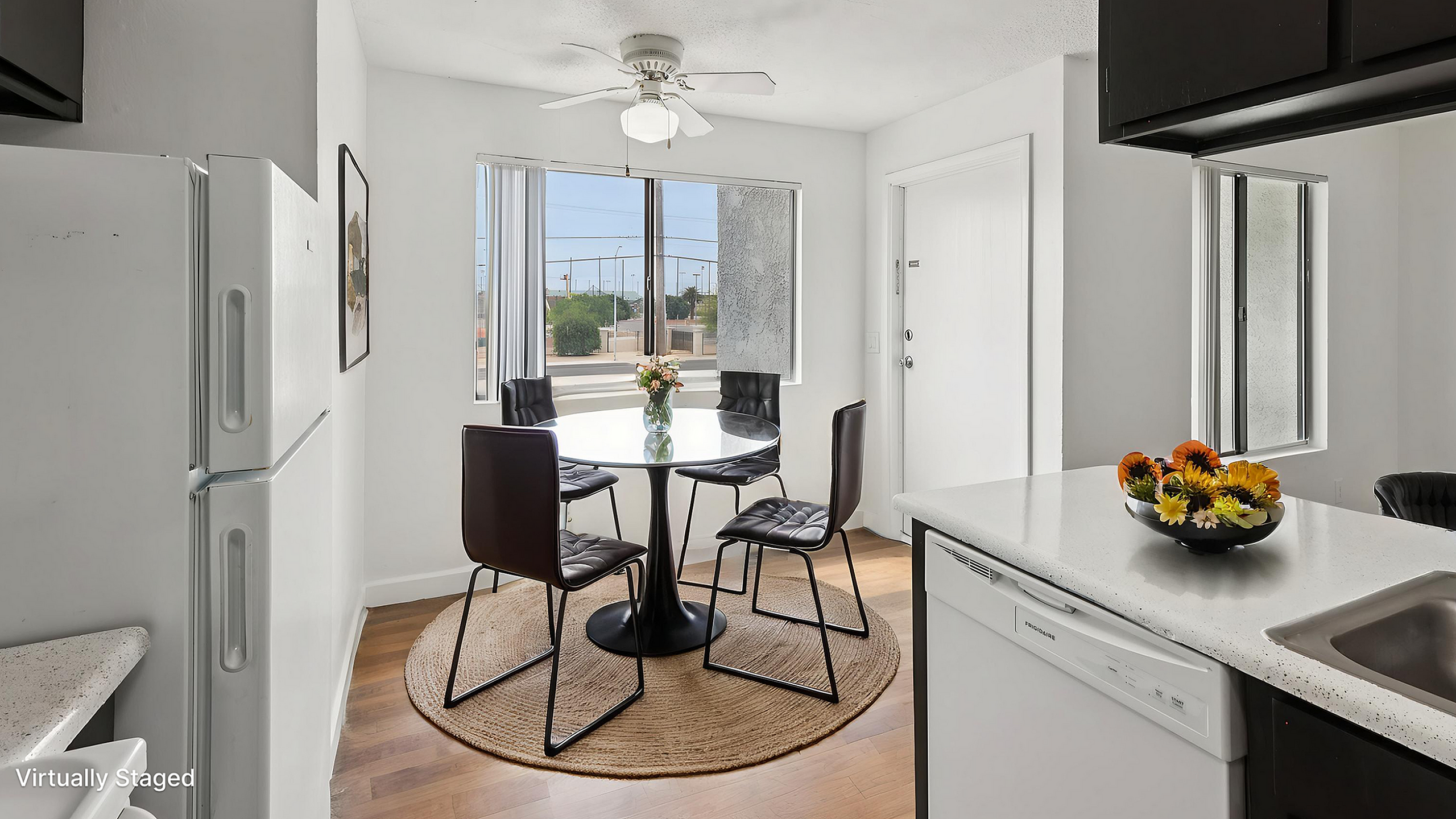 Bright and welcoming dining area in a modern apartment, featuring a stylish round table with four chic chairs, abundant natural light from large windows, and a cozy ambiance accentuated by fresh flowers.