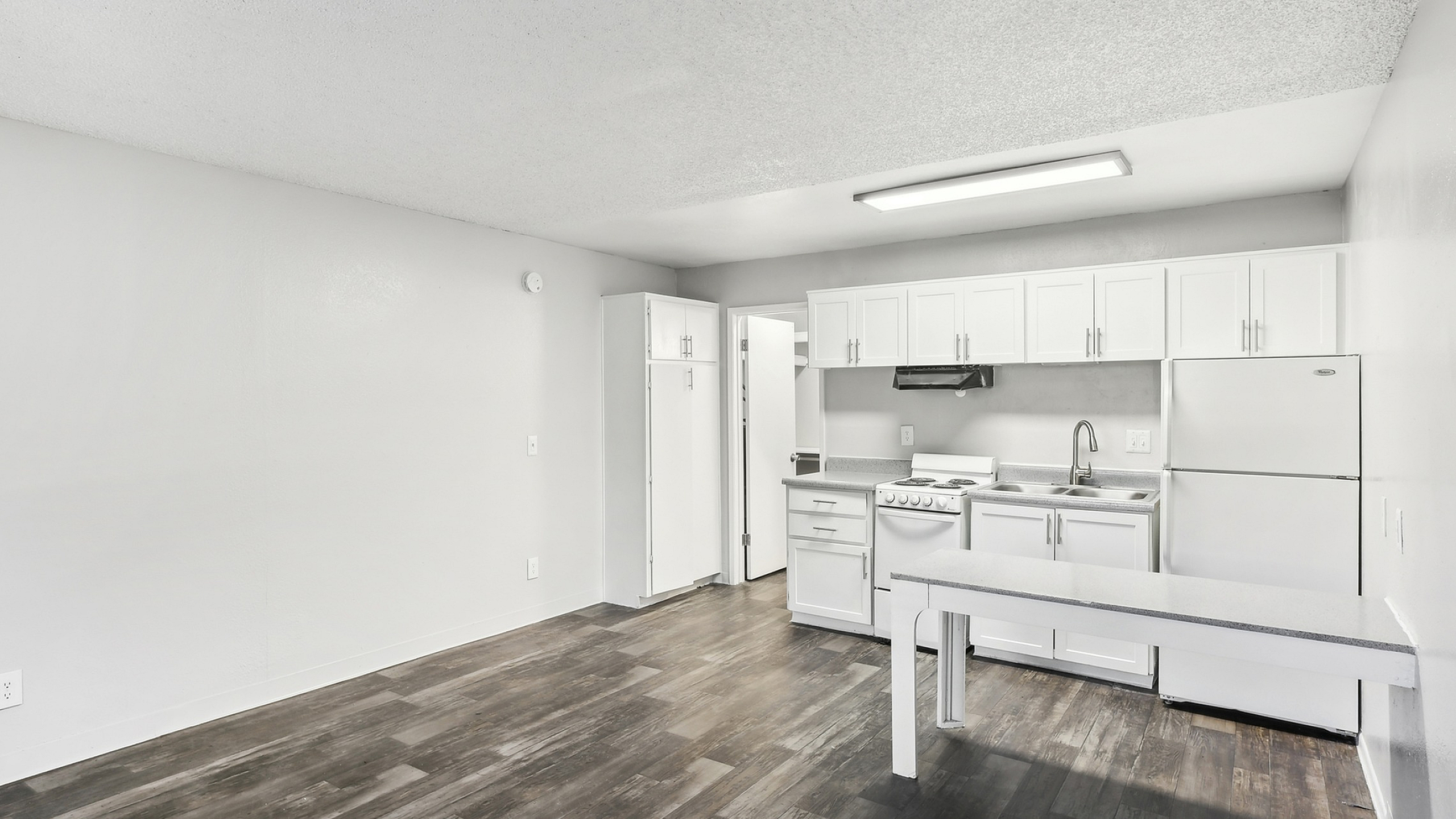 Modern apartment kitchen boasting sleek white cabinetry, a spacious countertop, and contemporary flooring in an open, airy layout.