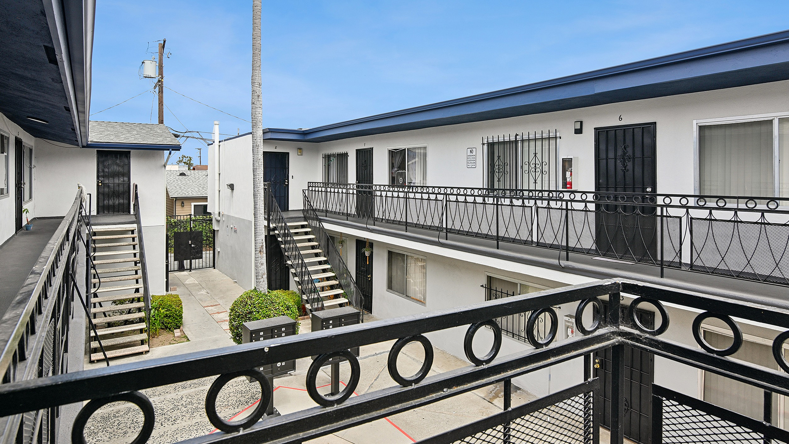 Charming apartment complex with stylish black railings and lush greenery, offering a serene urban living experience under a clear blue sky.