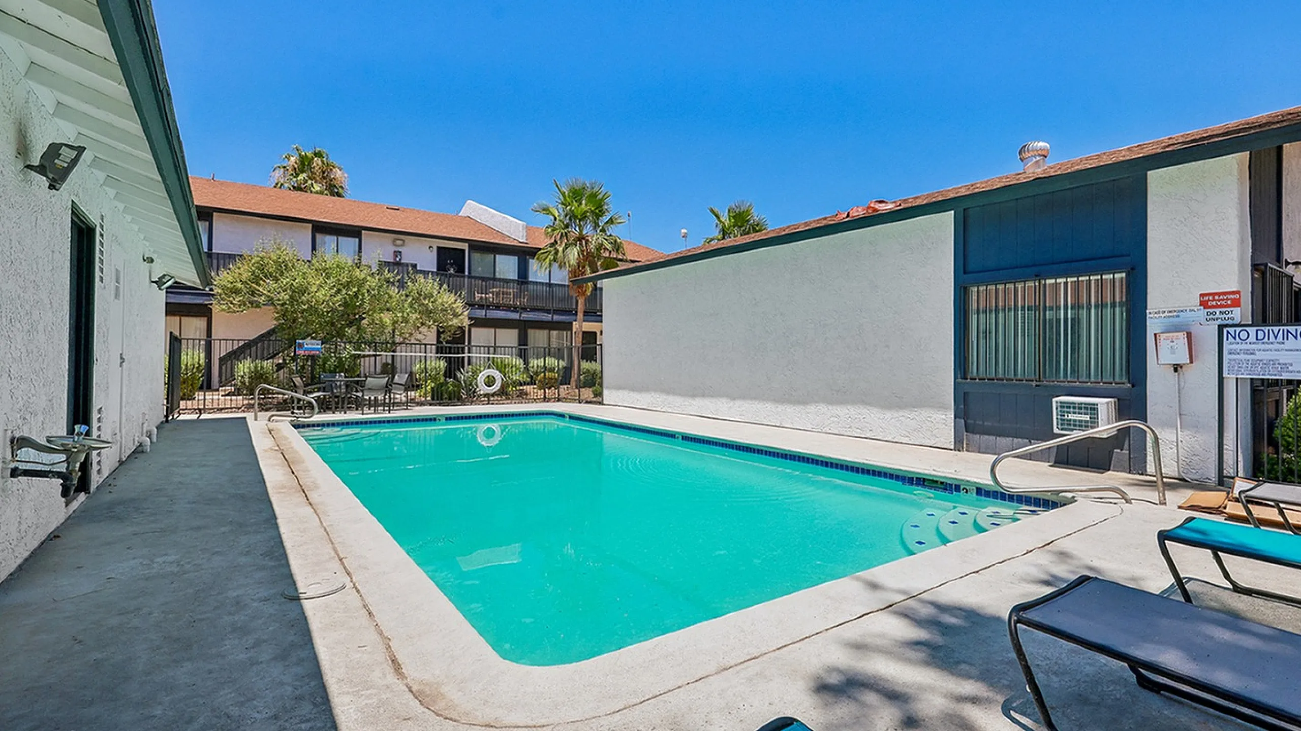 Inviting outdoor swimming pool with sun loungers, surrounded by well-maintained apartment buildings and lush palm trees, capturing a serene and relaxing ambiance.