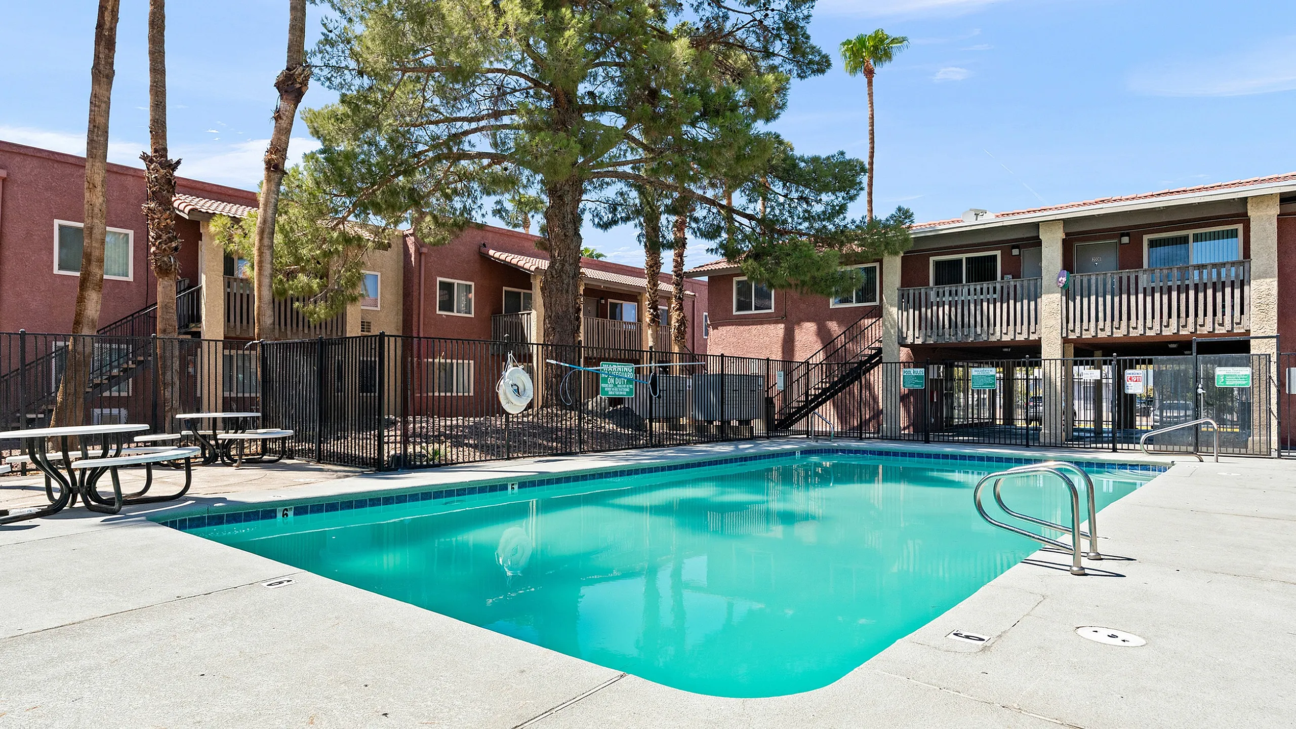 Inviting apartment complex with a beautiful pool, surrounded by lush trees and outdoor seating, perfect for relaxation and leisure.