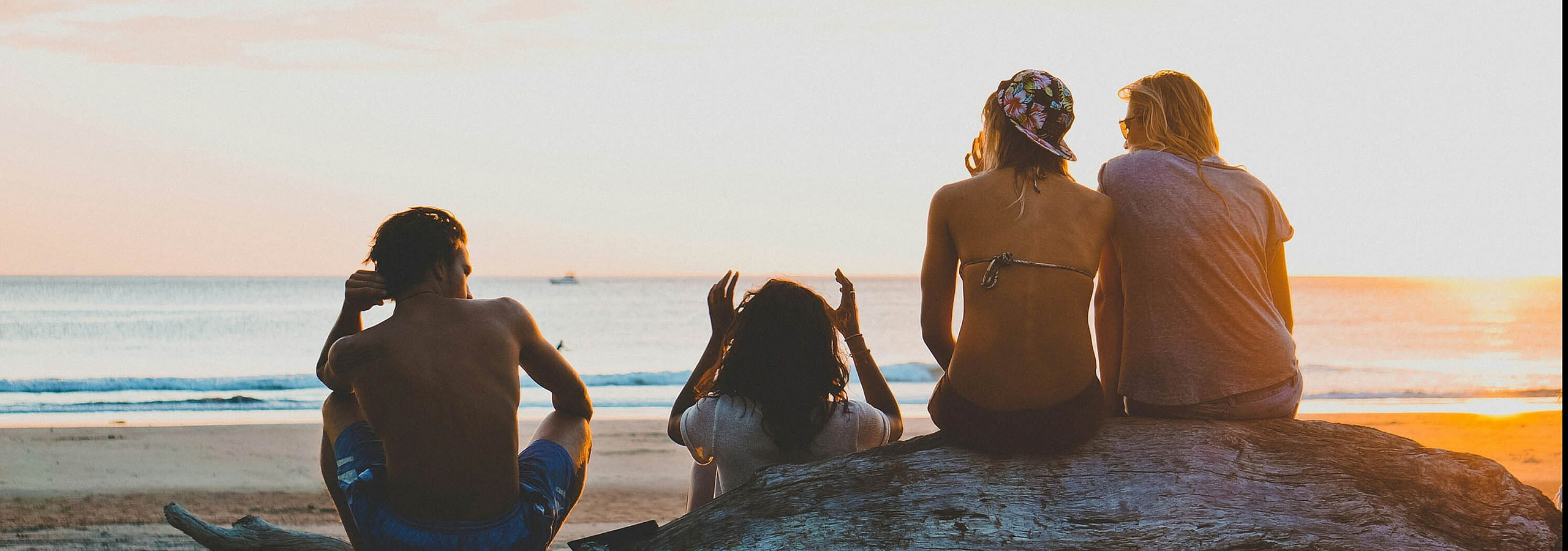 four people at the beach sitting on a boulder