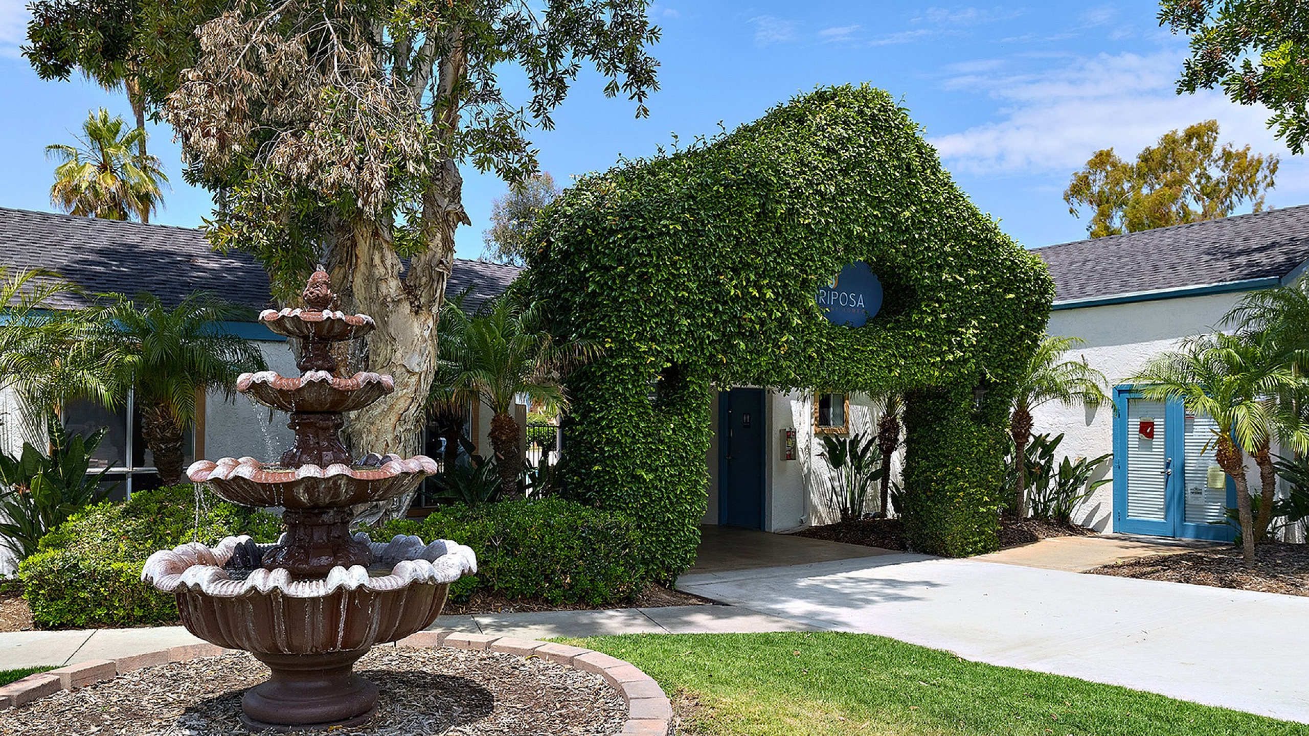 Property entrance with fountain and greenery with blue skies.