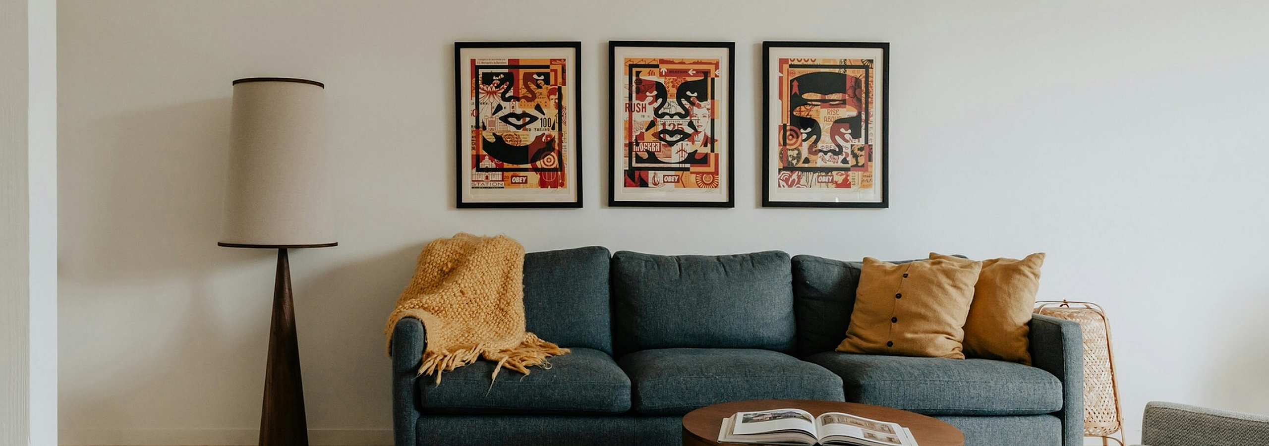blue sofa with yellow accent pillows and three obey giant prints behind