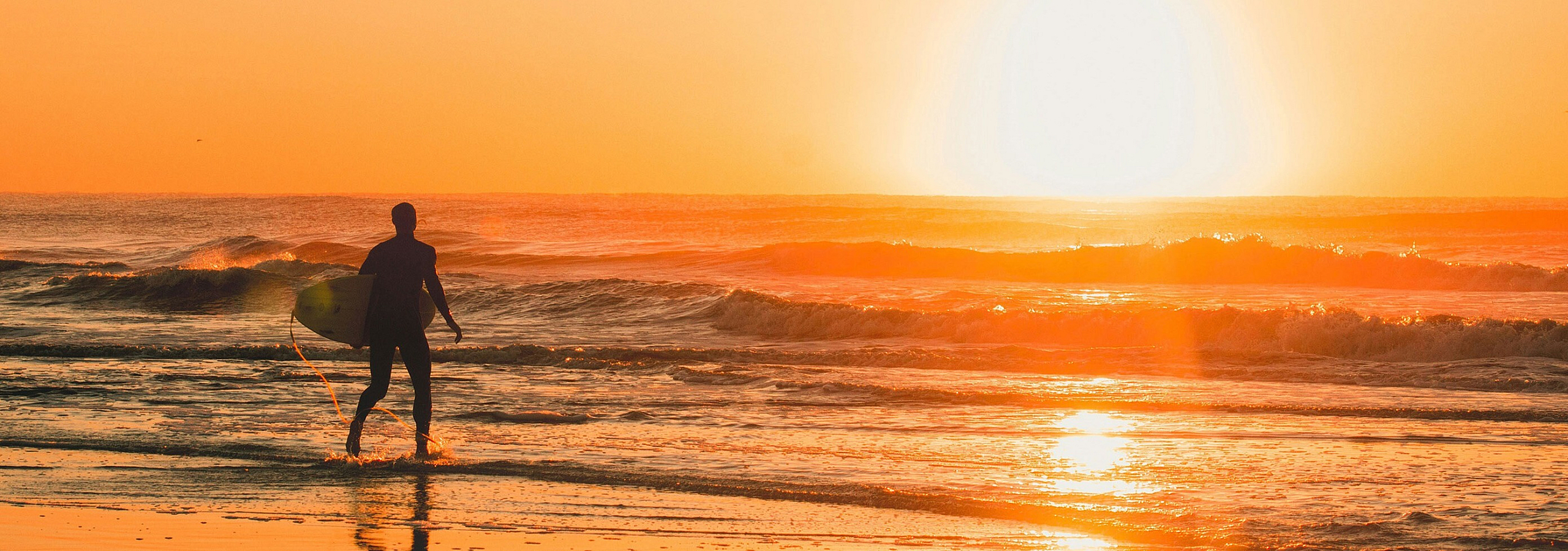 man walking with surfboard at sunset