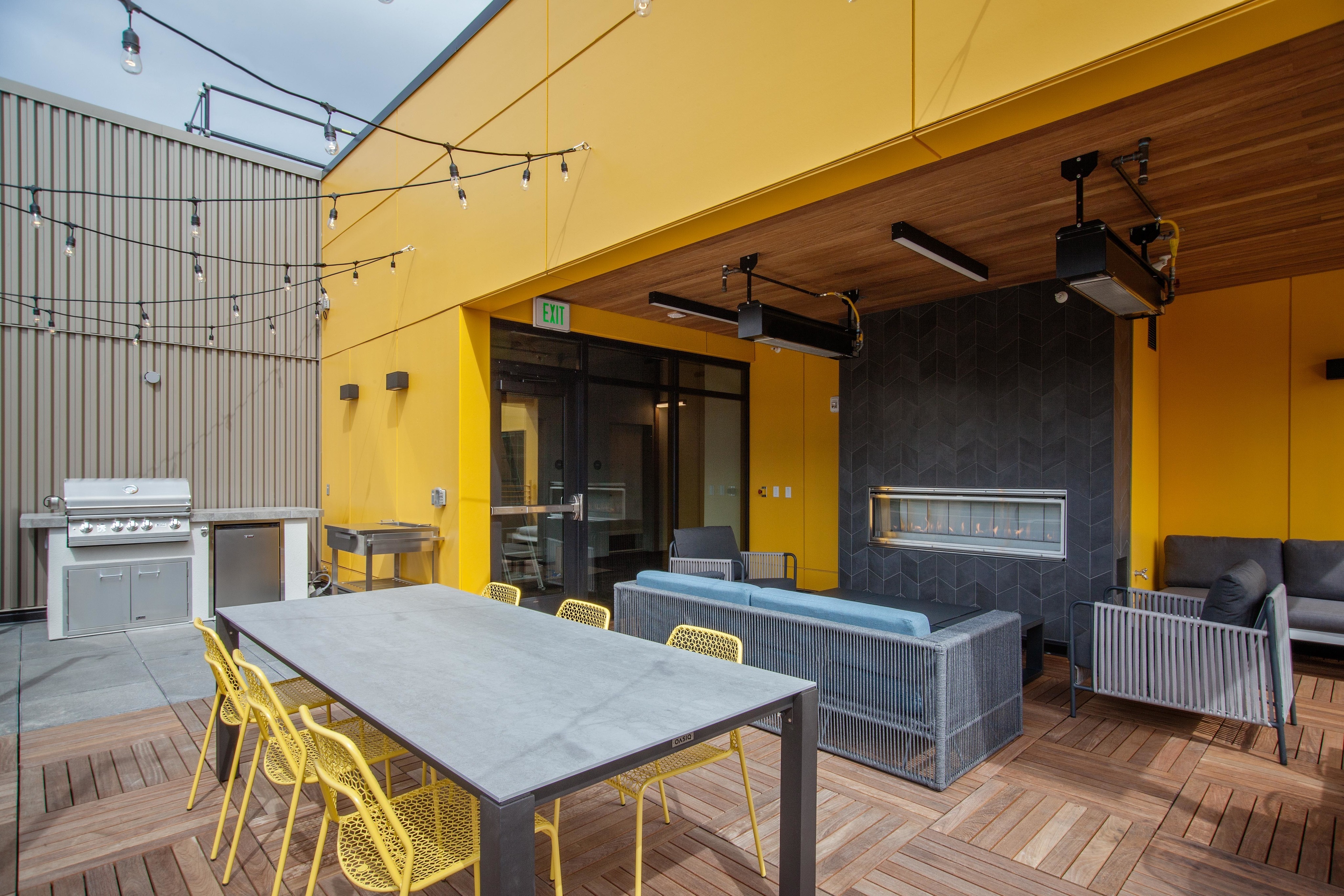 Slabtown OR Apartments - ORO - Rooftop Lounge With Fireplace, Plush Seating, Chairs, Tables, String Lights, And BBQ Grill.