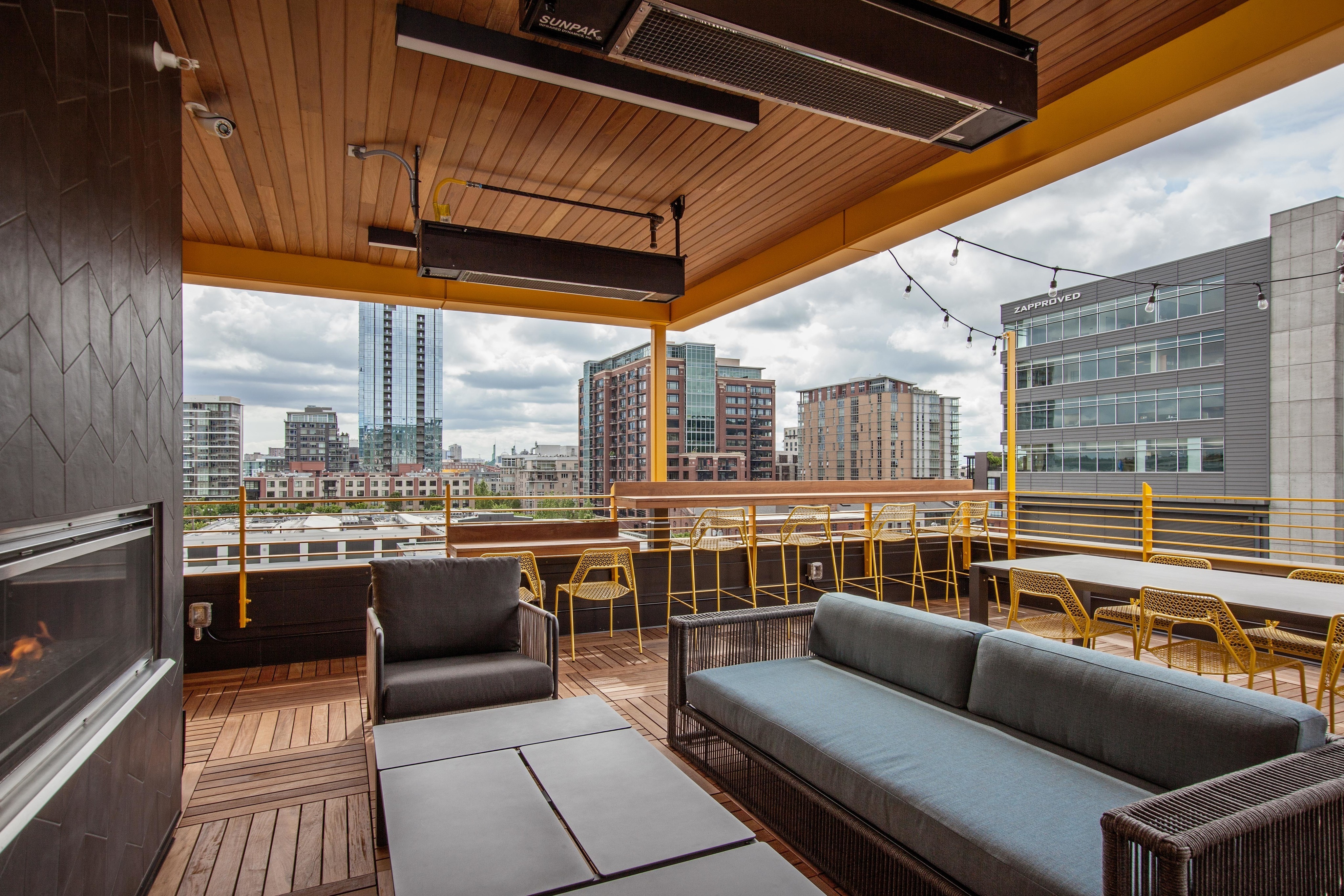 Downtown Portland OR Apartments Near Portland State University - ORO - Rooftop Lounge With Fireplace, Plush Seating, Chairs, Tables, String Lights, And Panoramic City Views.
