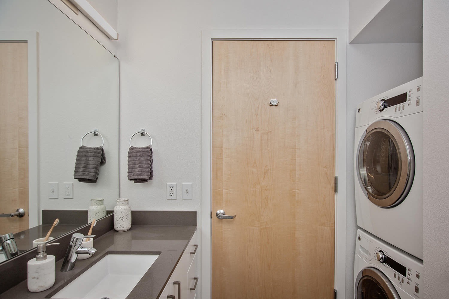Slabtown, OR Apartments For Rent - ORO - Bathroom With In-Unit Washer And Dryer, A Vanity With A Large Mirror, White Cabinets, And A Grey Countertop