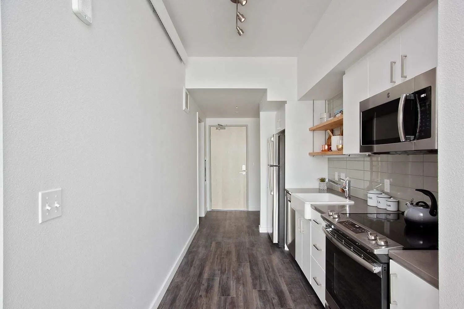 Studio Apartments in Downtown Portland OR - ORO - An interior shot of the kitchen featuring Stainless Steel Appliances, Grey Countertops, White Cabinetry, Wood-Style Flooring, and Tile Backsplash