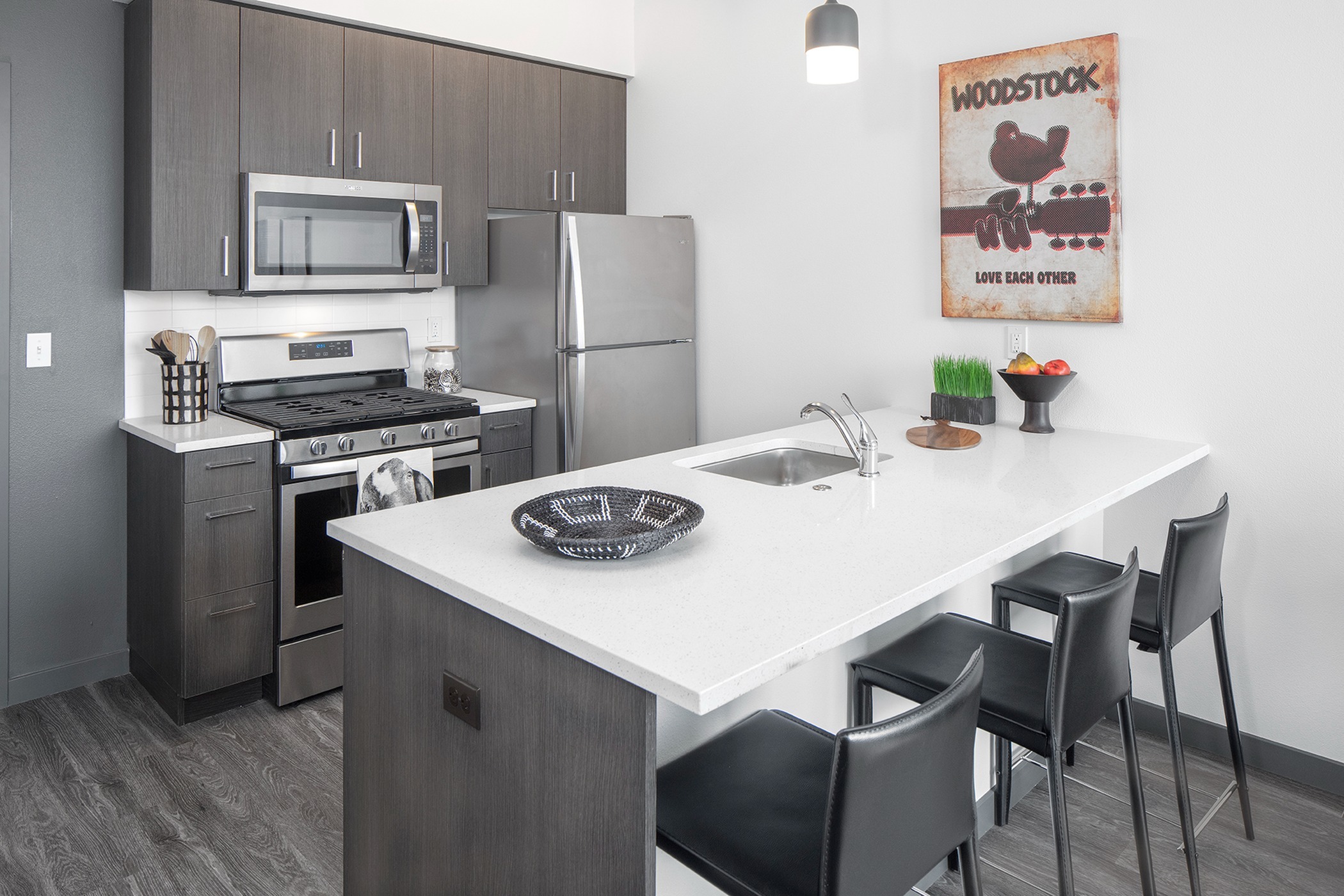 Apartments For Rent Williams District, OR - Kitchen With Breakfast Bar, Quartz Counters, Stainless-Stell Appliances, And Vinyl Wood Flooring.