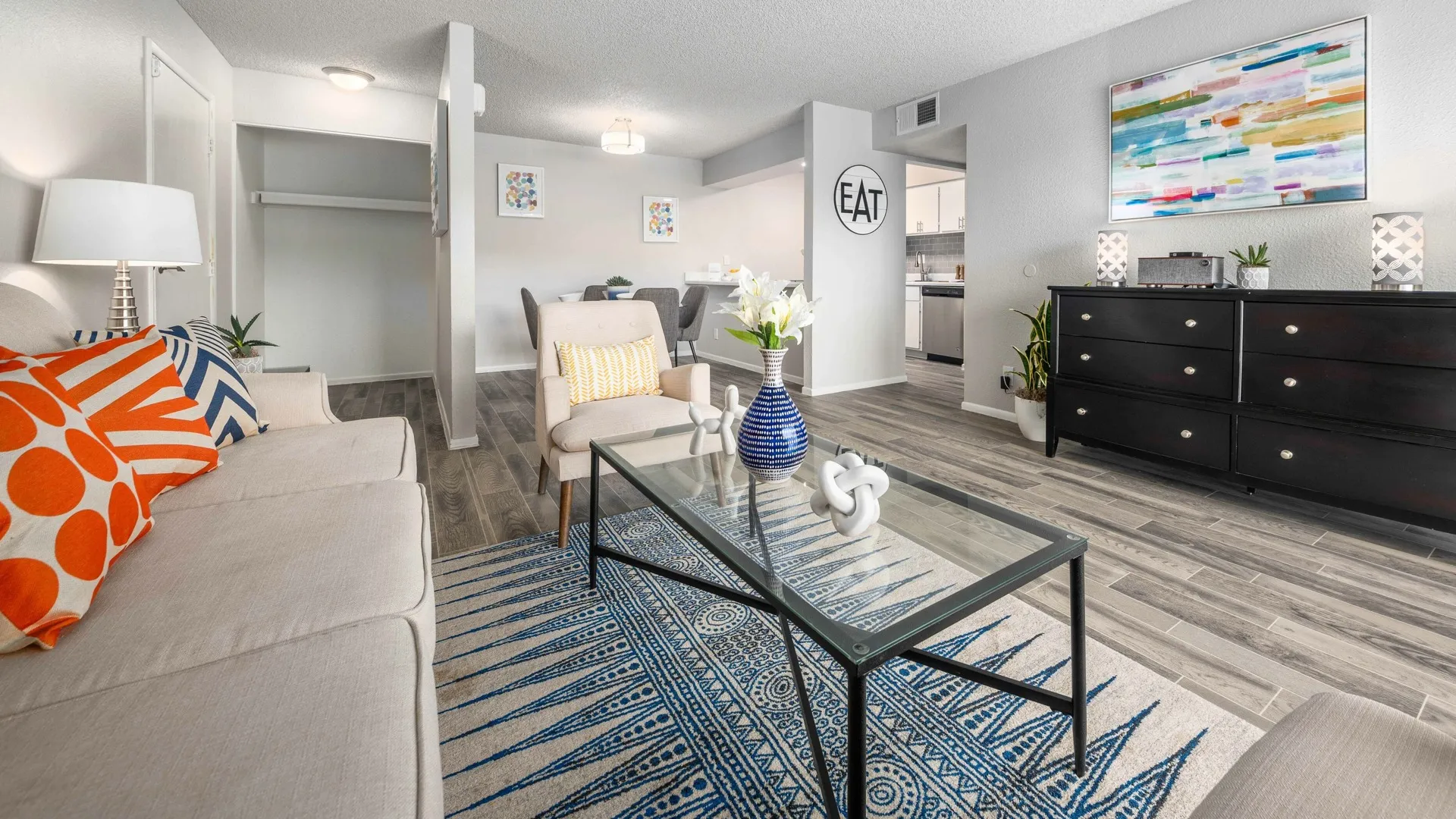 living room with faux hardwood flooring a black console, a glass and metal coffee table and a taupe sofa and arm chairs at peoria grand apartments