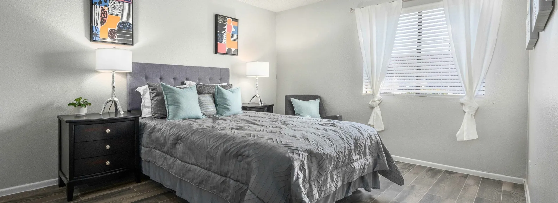 bedroom with faux hardwood flooring, two bedside nightstands and a bed with a grey cover at peoria grand apartments