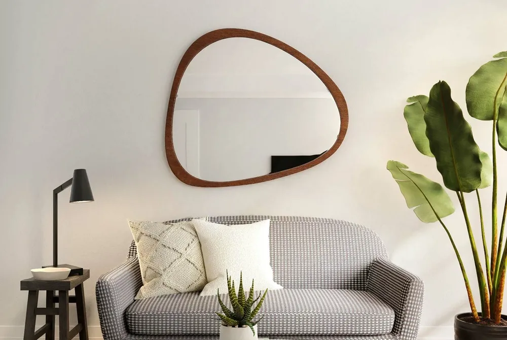 sofa with accent pillows and a stool being used as a side table with a lamp and an oddly rounded mirror with a wooden frame