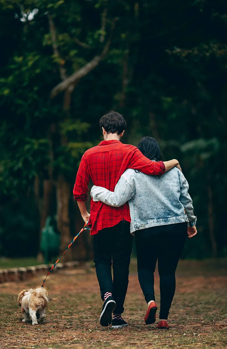two people walking together embraced with their dog on a leash