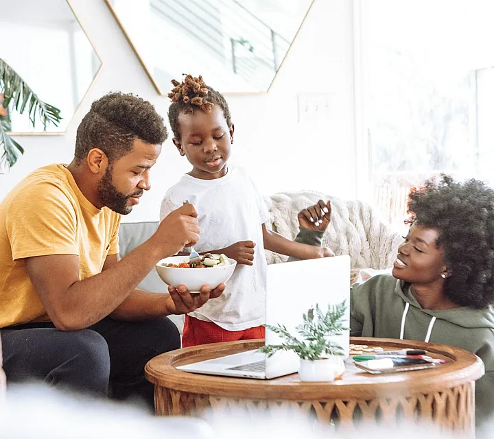 two adults and child sharing a bowl of food in living room