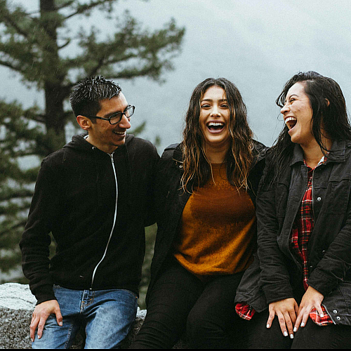 three people laughing while sitting on a ledge