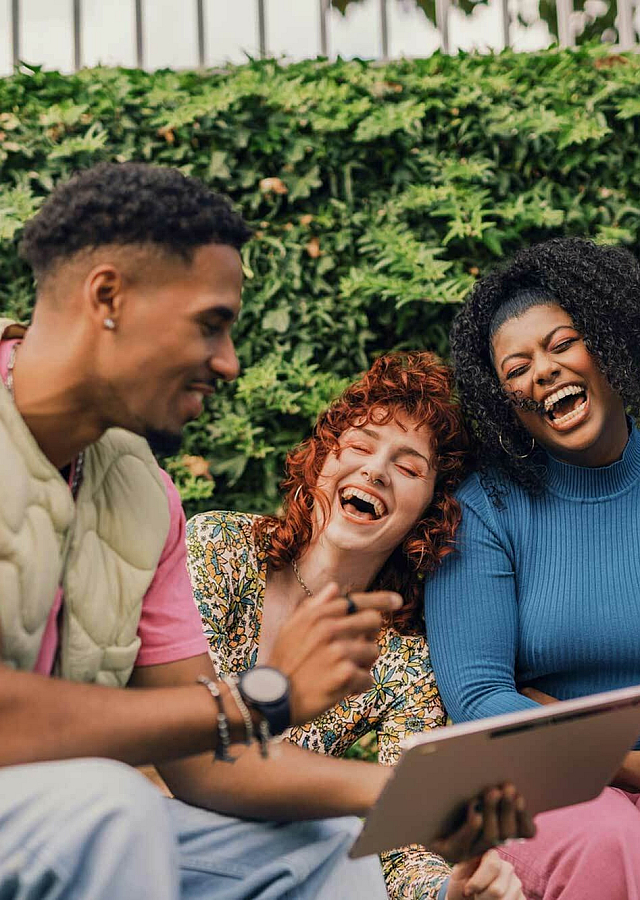three people laughing while looking at a tablet