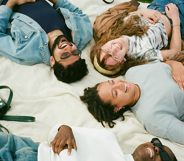 four friends laying on the ground looking up at the sky laughing