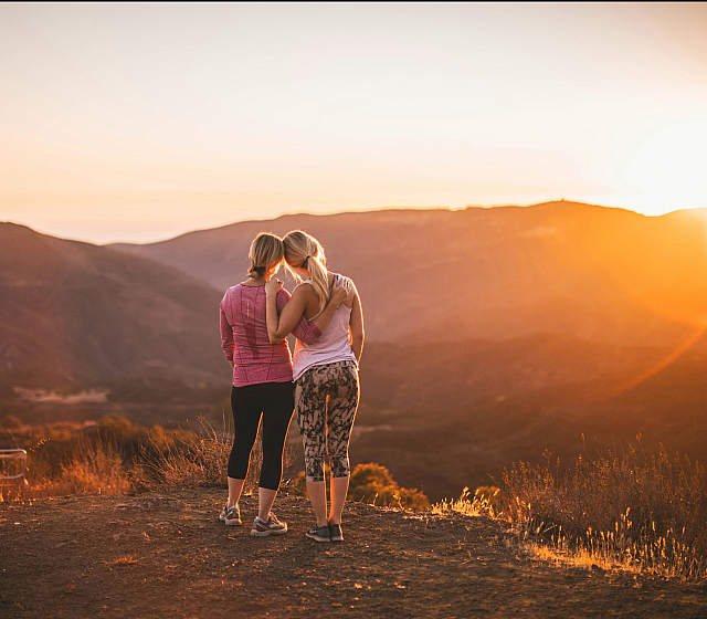 two women looking at the sunset at the top of a hill