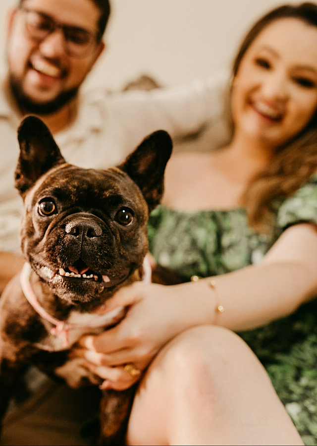 two people sitting on a sofa with their small dog in the middle