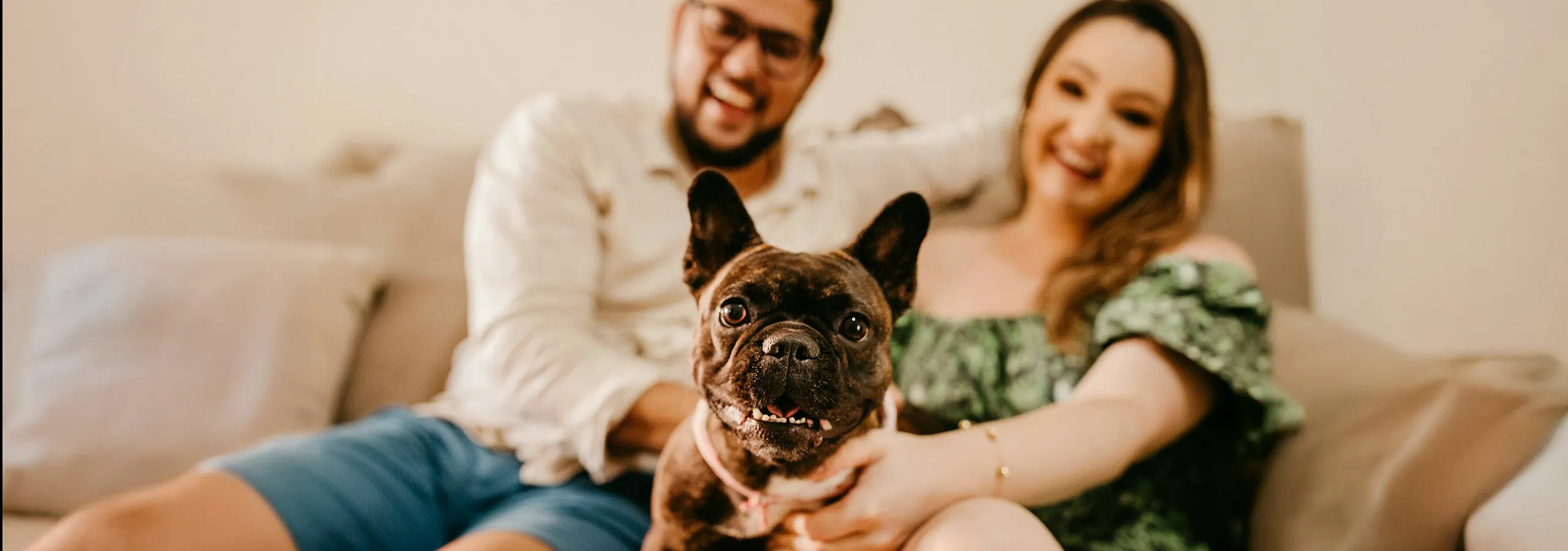 two people sitting on a sofa with their small dog in the middle