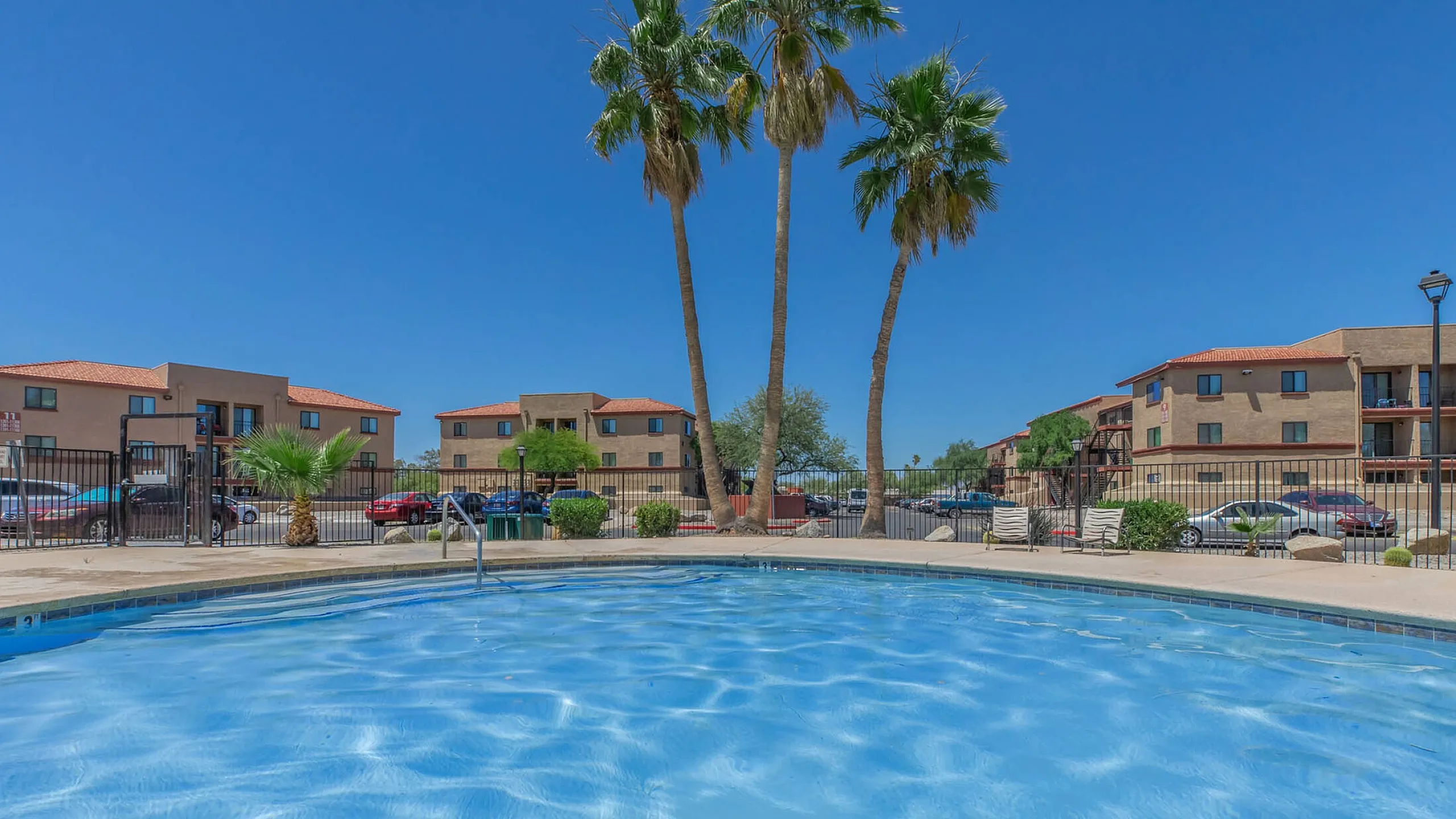 pool with three palm trees in the background and three story apartment buildings further back